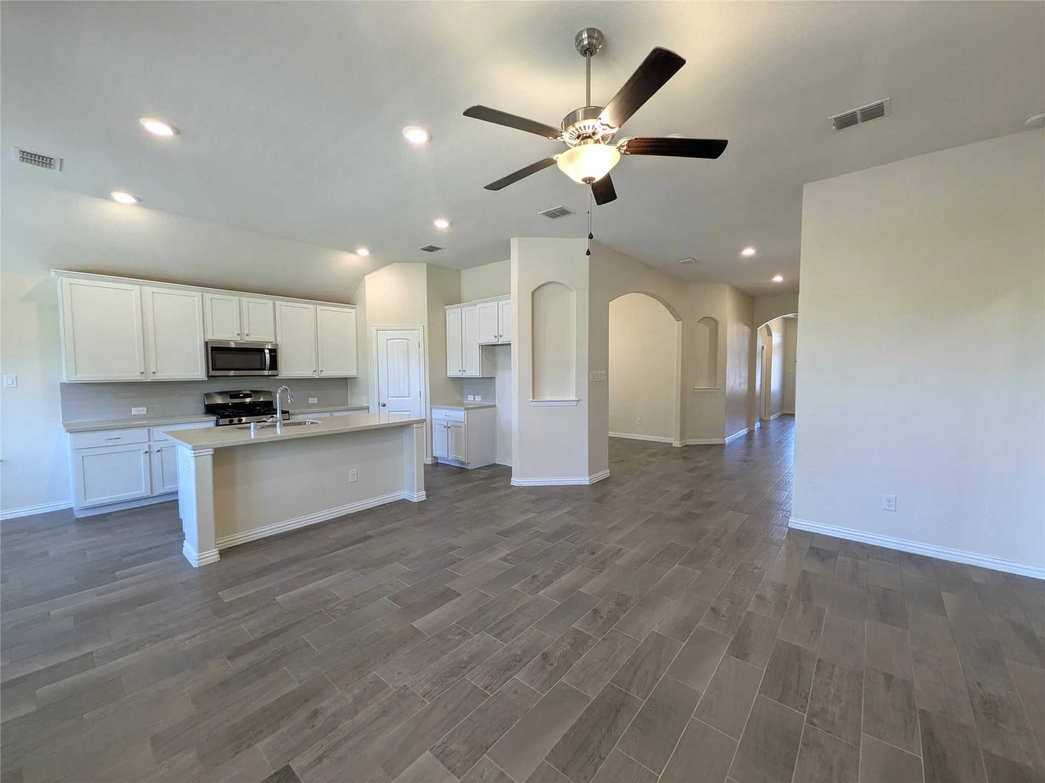 Open-concept living space featuring gleaming wood-finish flooring throughout, white cabinetry with stainless steel appliances, recessed ceiling lighting, and a ceiling fan with integrated light fixture