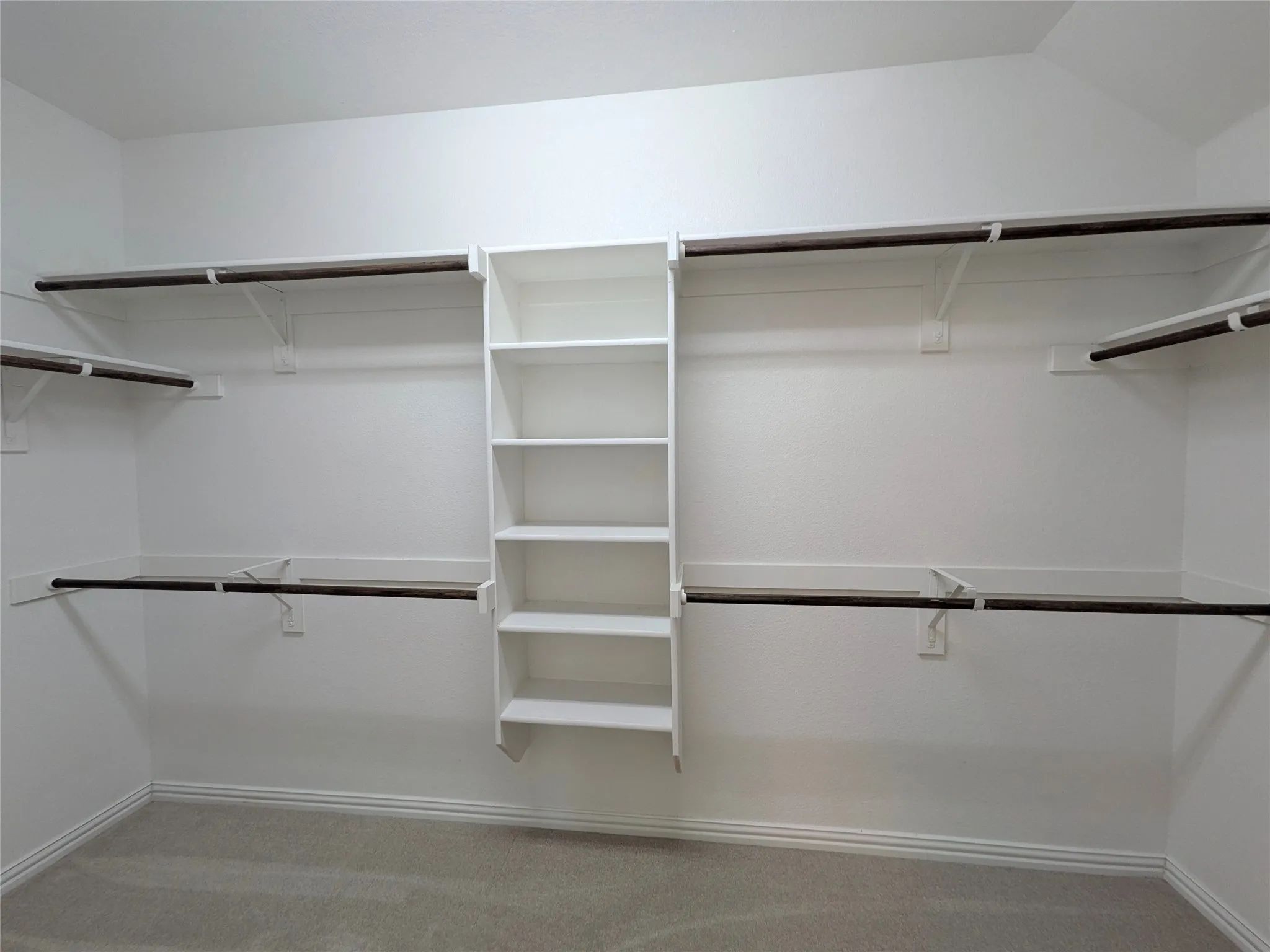 Spacious walk-in closet featuring light gray carpet, white baseboards, and white walls