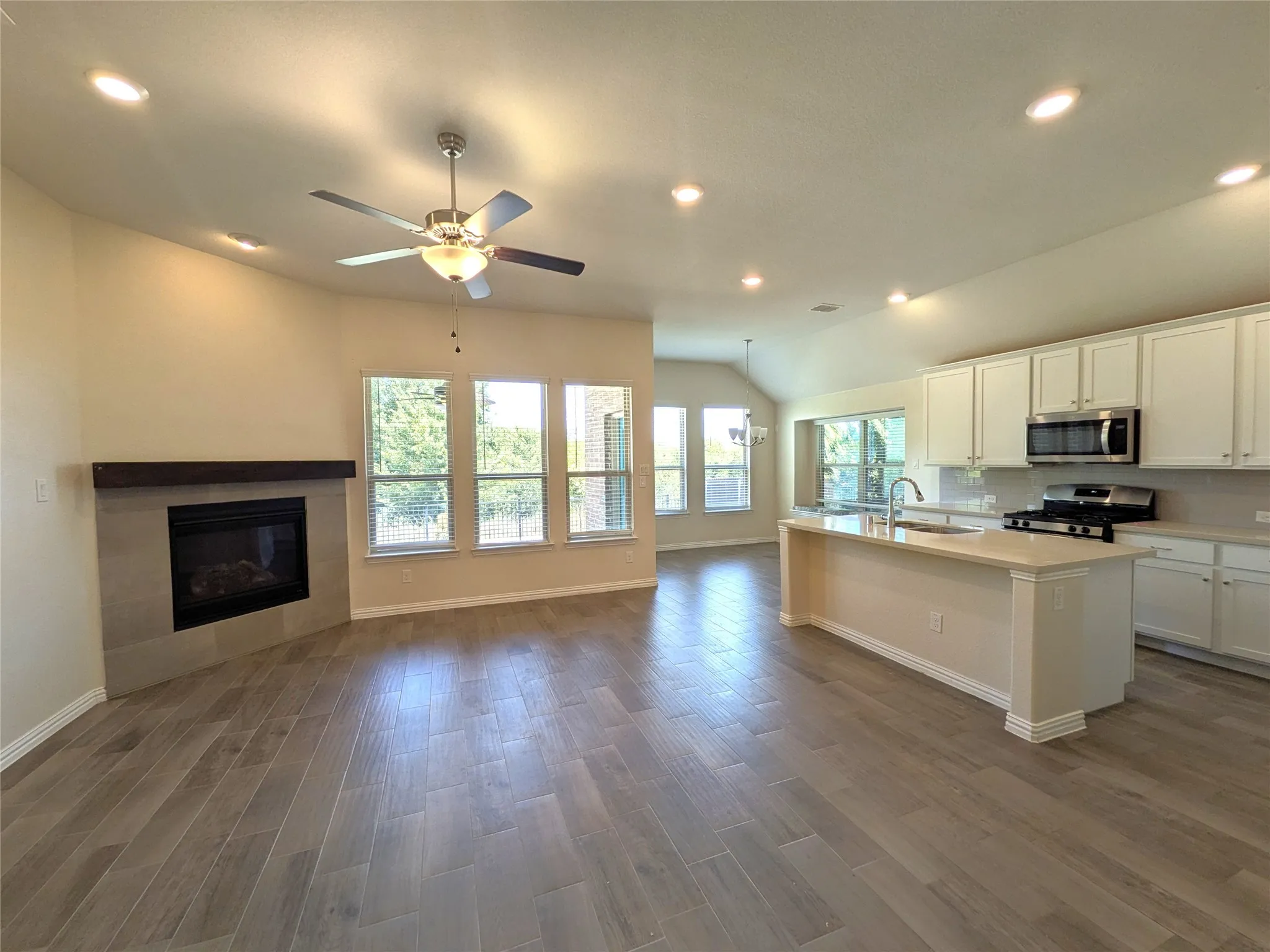 Open-concept living space featuring wood-finish flooring throughout, a ceiling fan with integrated lighting, and recessed lighting