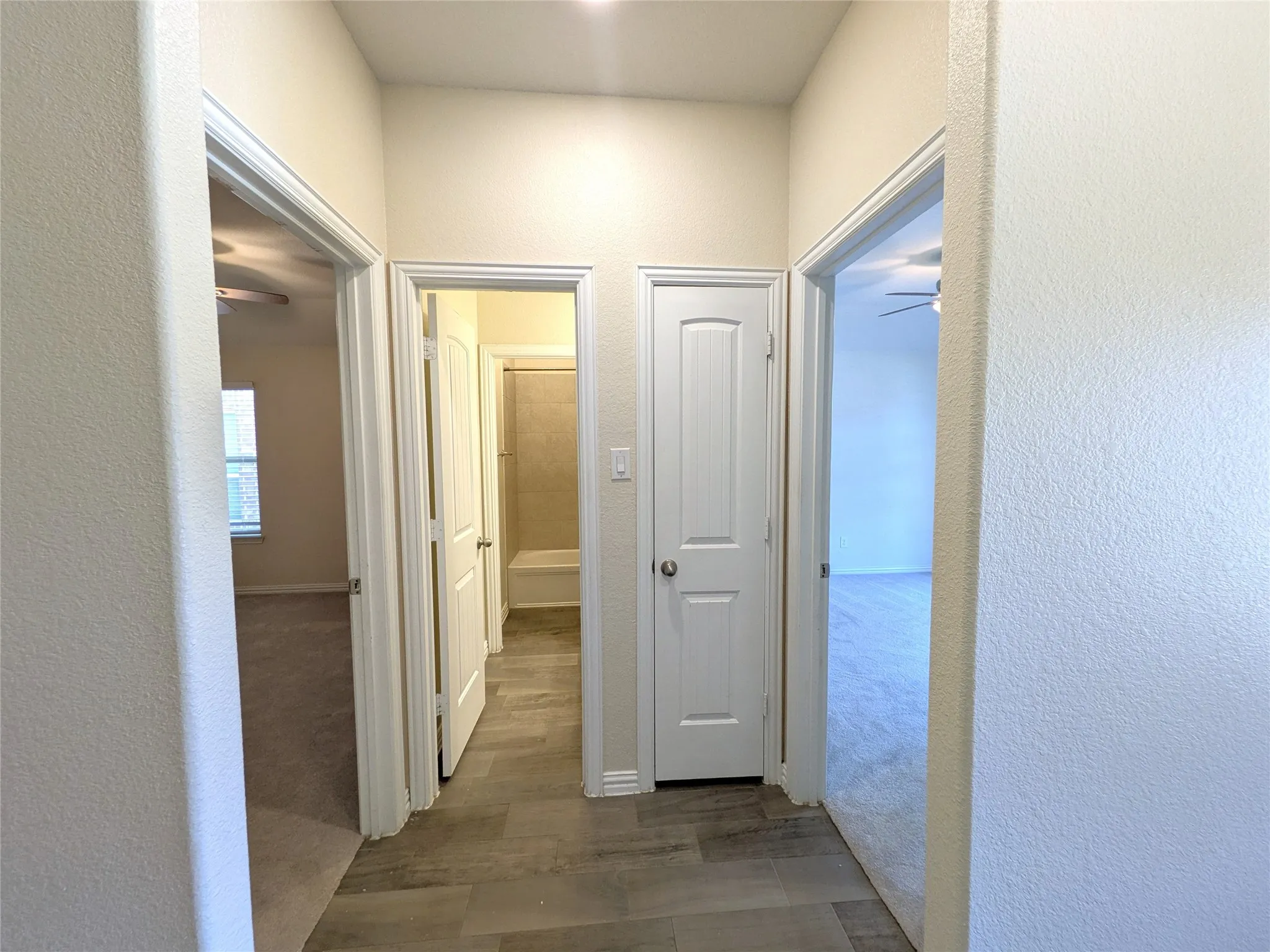 Efficient hallway layout featuring multiple white six-panel doors, wood-finish flooring throughout, and bright overhead lighting