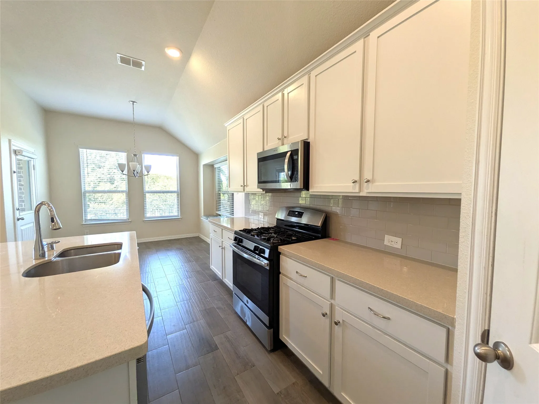 Galley kitchen featuring cream cabinetry with recessed panel doors, stainless steel appliances including a gas range and microwave, quartz countertops, subway tile backsplash, undermount sink with chrome faucet, and wood-finish flooring throughout