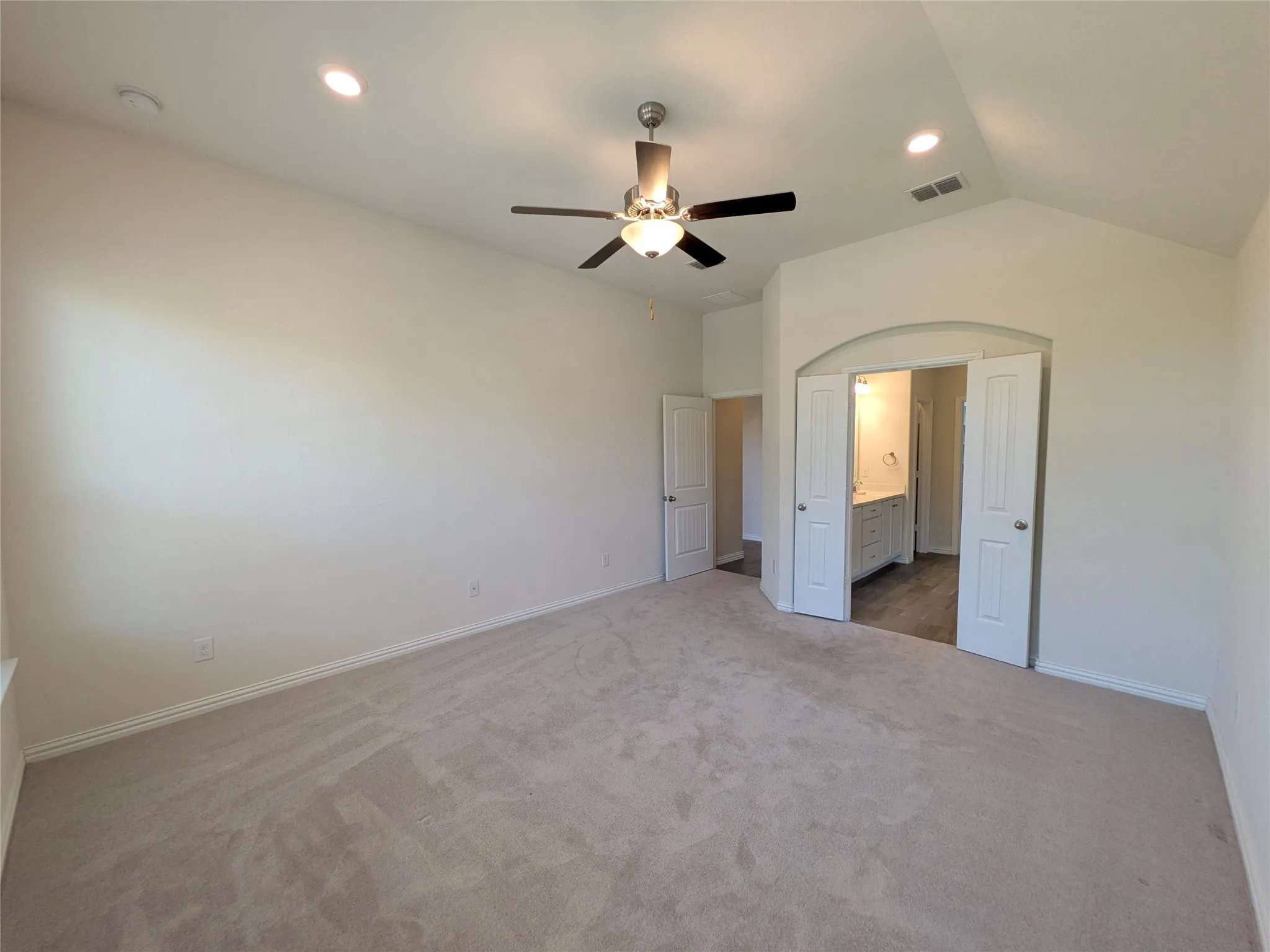 Spacious carpeted room featuring a vaulted ceiling with recessed lighting and a ceiling fan