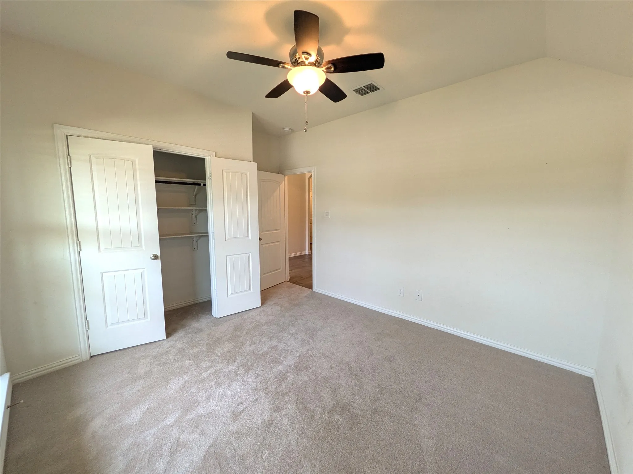 Carpeted room featuring a vaulted ceiling with a ceiling fan, a bi-fold closet with shelving, and light-colored walls