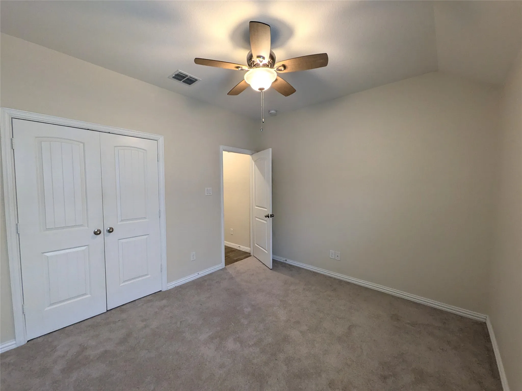 Neutral-toned bedroom featuring a ceiling fan with light fixture, light gray carpeting, white trim, and a double closet with panel doors