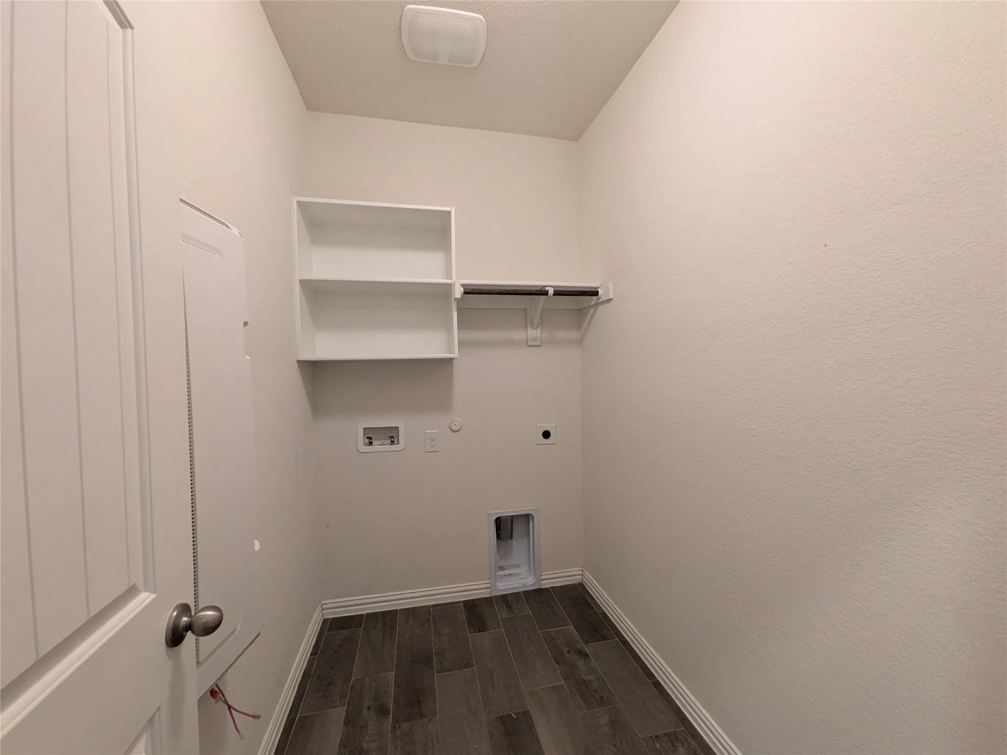 Dedicated laundry room featuring white shelving and rod storage, wood-finish flooring, and practical layout with utility outlet access