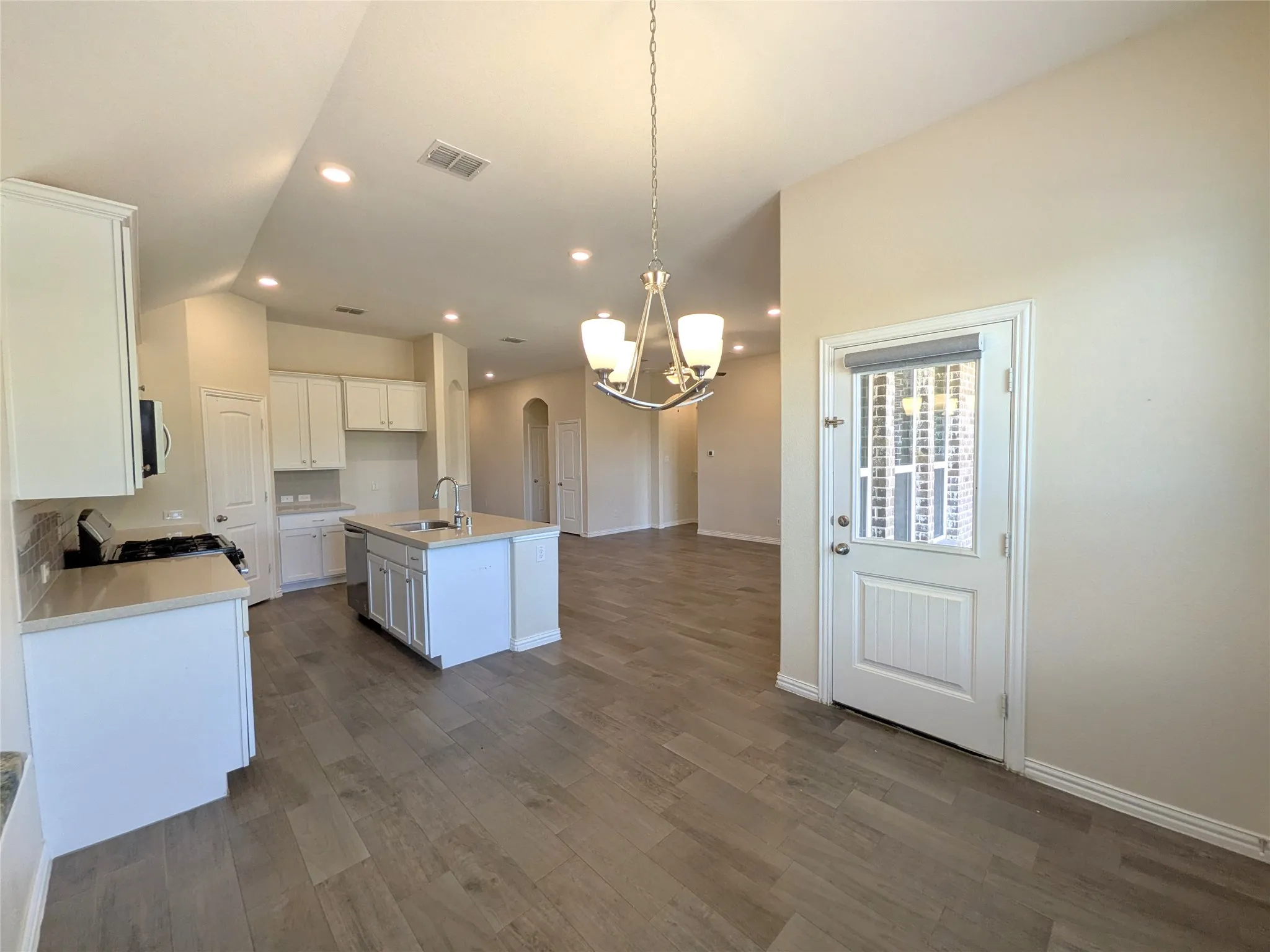 Open-concept kitchen and dining area featuring light wood-finish flooring, recessed lighting, and a contemporary chandelier