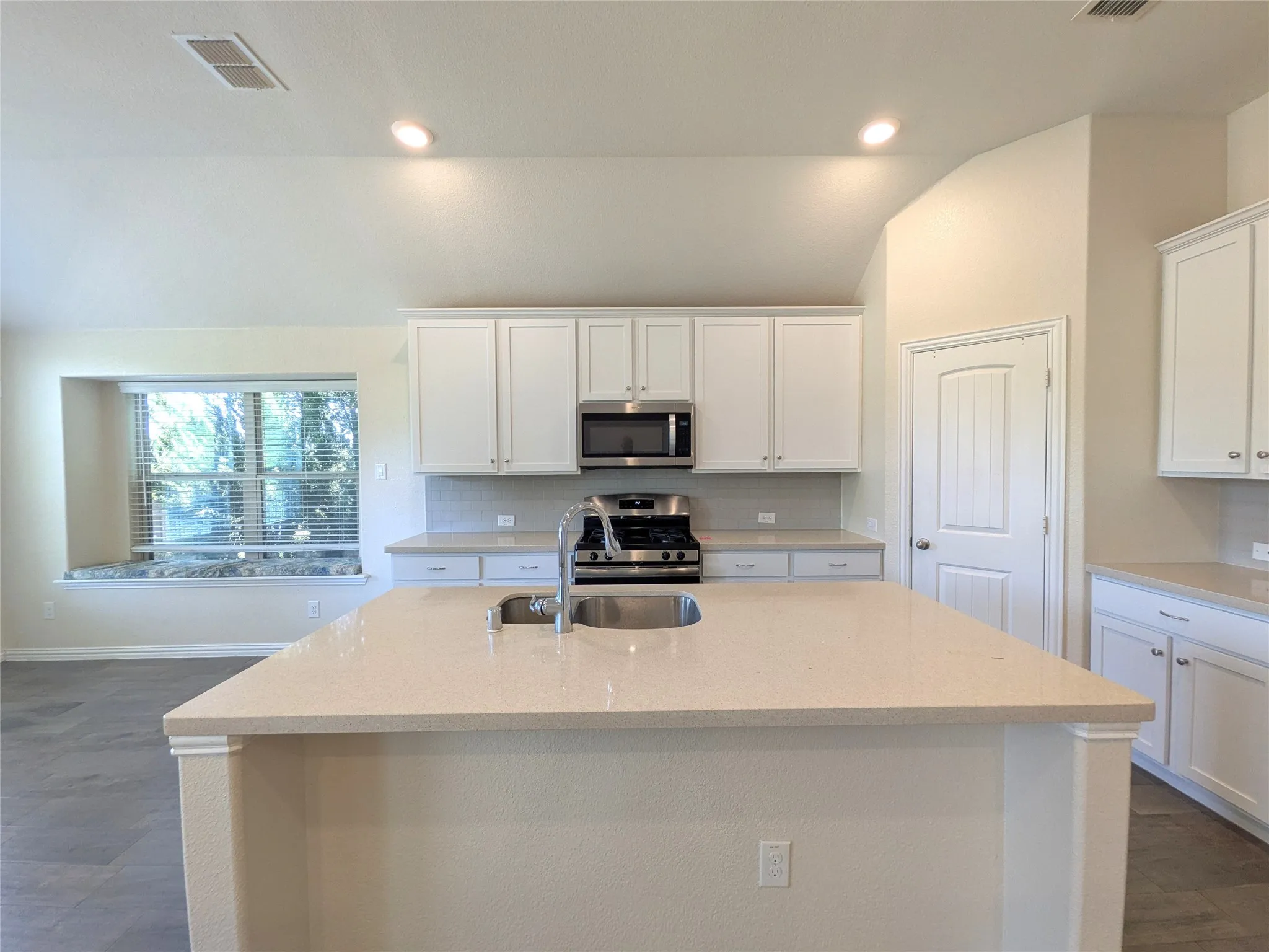Bright, open kitchen featuring white cabinetry, stainless steel gas range and microwave, quartz countertops, and a spacious island with seating
