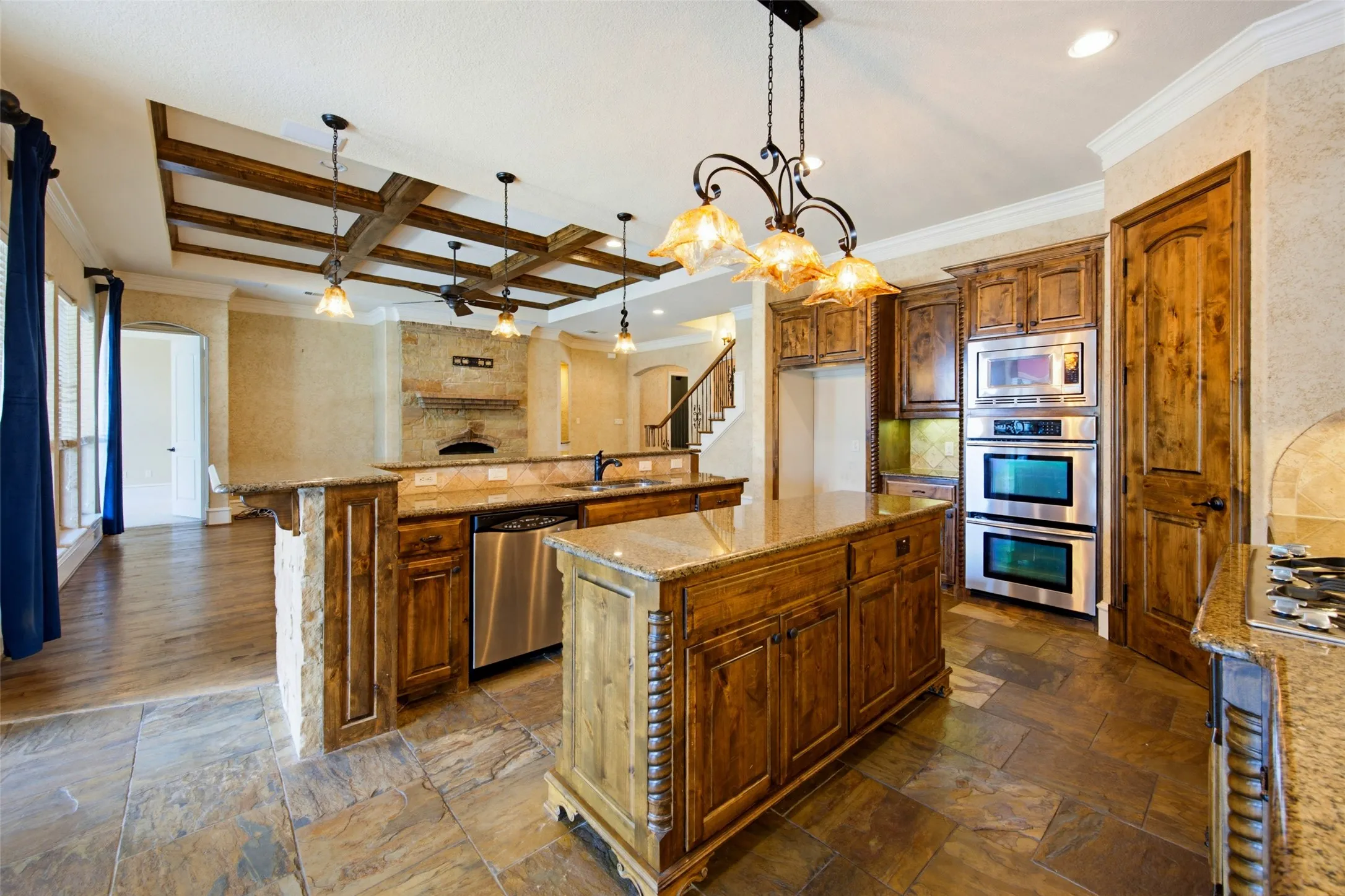 Kitchen featuring a large island with stone countertops, integrated stainless steel appliances, rich wood cabinetry, and stone tile flooring