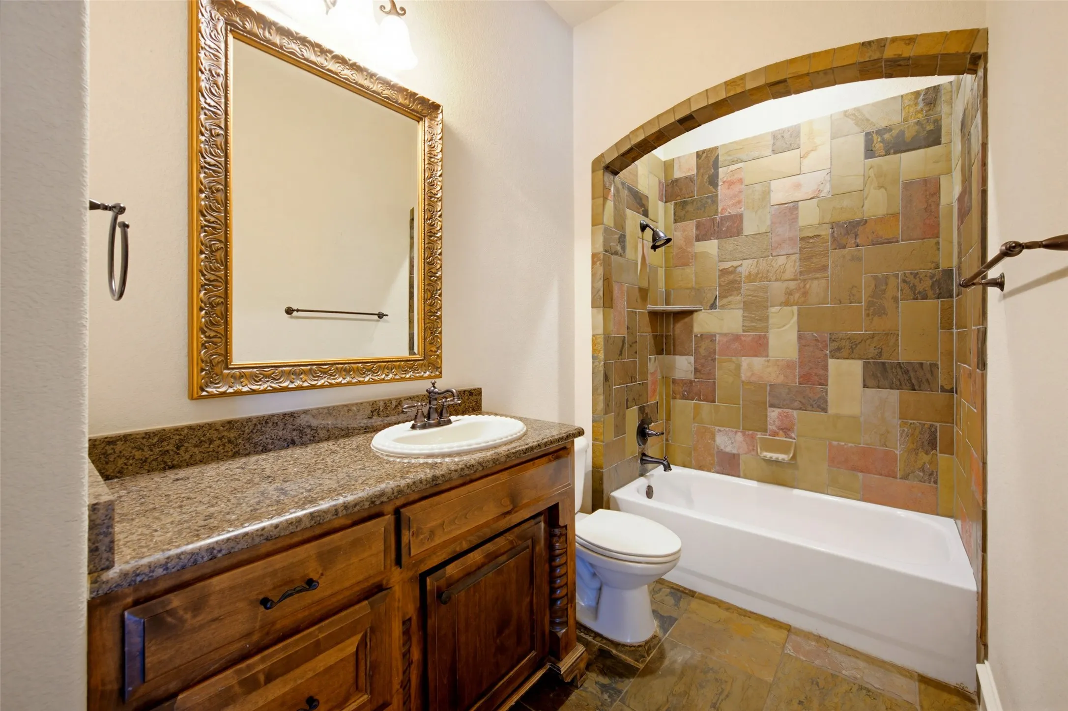 1st level guest suite full bath featuring a wood-finish vanity with granite countertop, vessel sink, and ornate framed mirror
