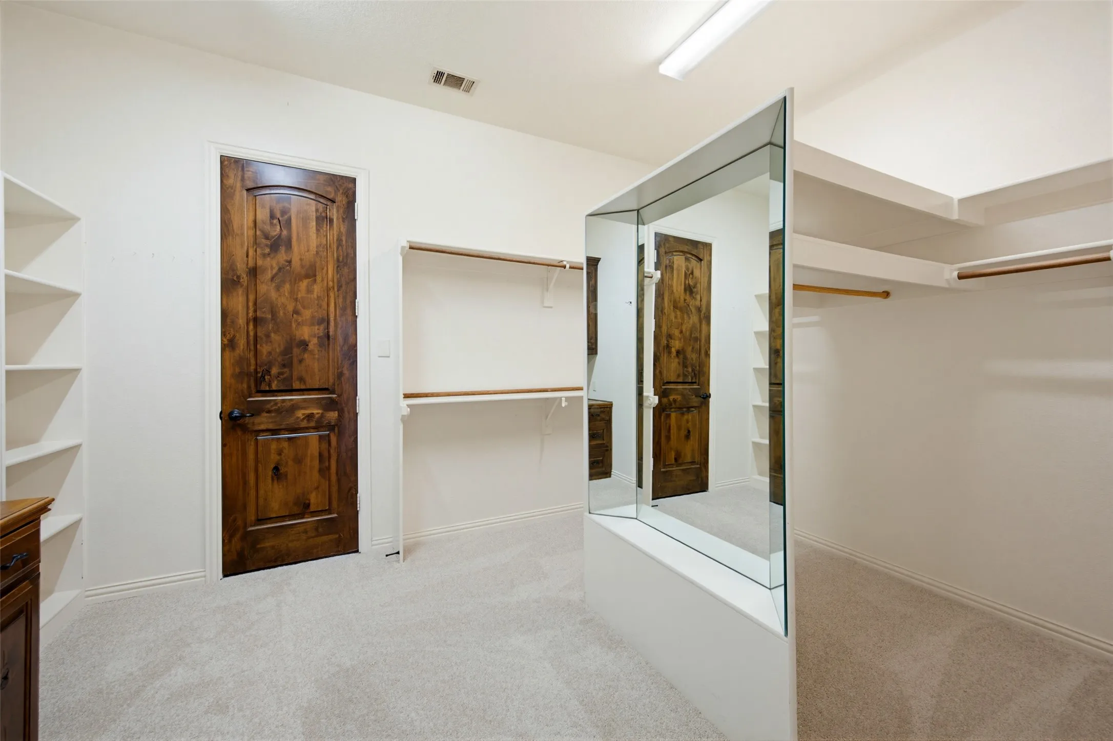 Spacious primary walk-in closet featuring custom shelving, glass-front cabinetry with wood-finish doors, recessed lighting, and carpeted flooring