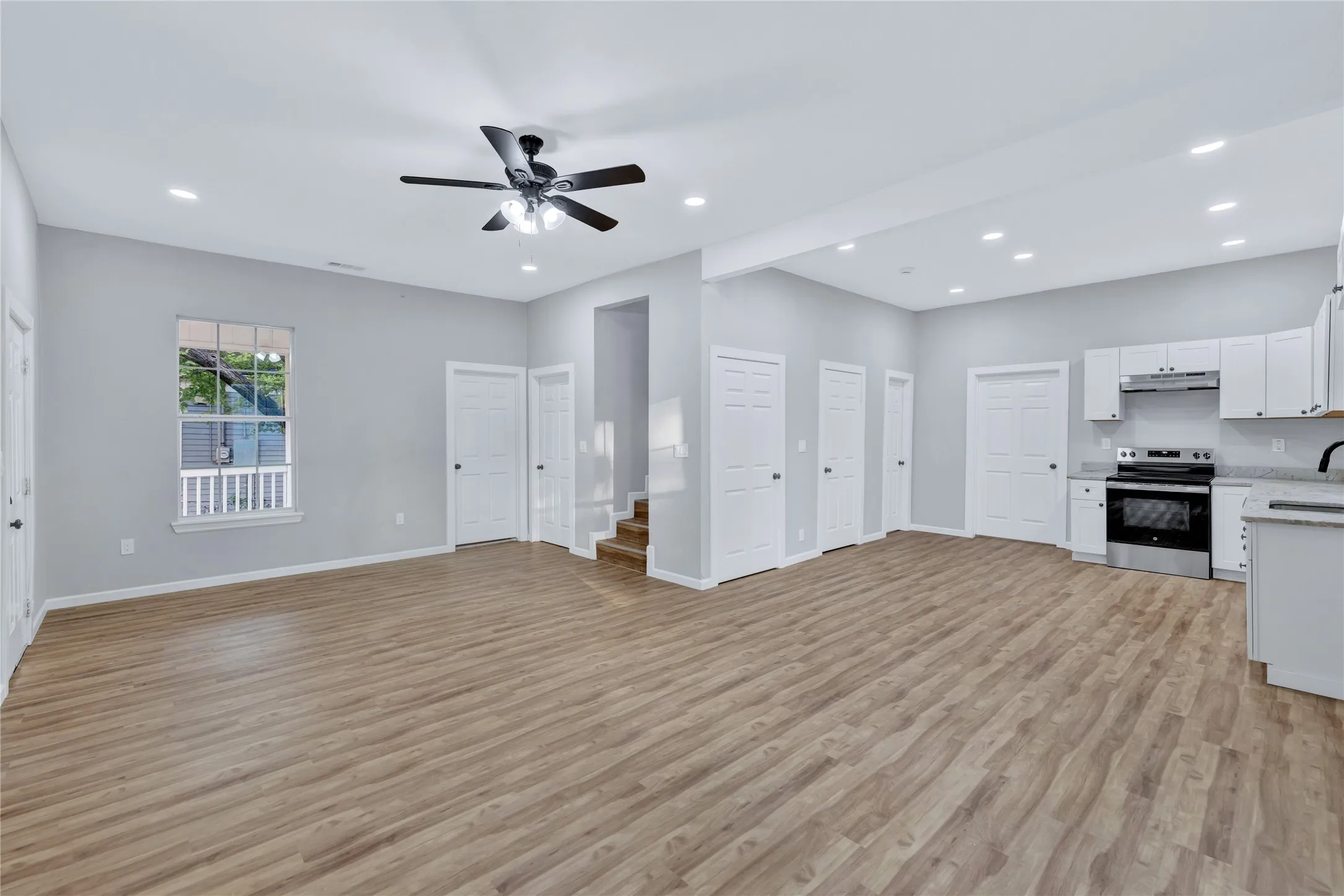 Open-concept living space featuring wood-finish flooring, recessed lighting, a ceiling fan, and a kitchen with white cabinetry and stainless steel appliances