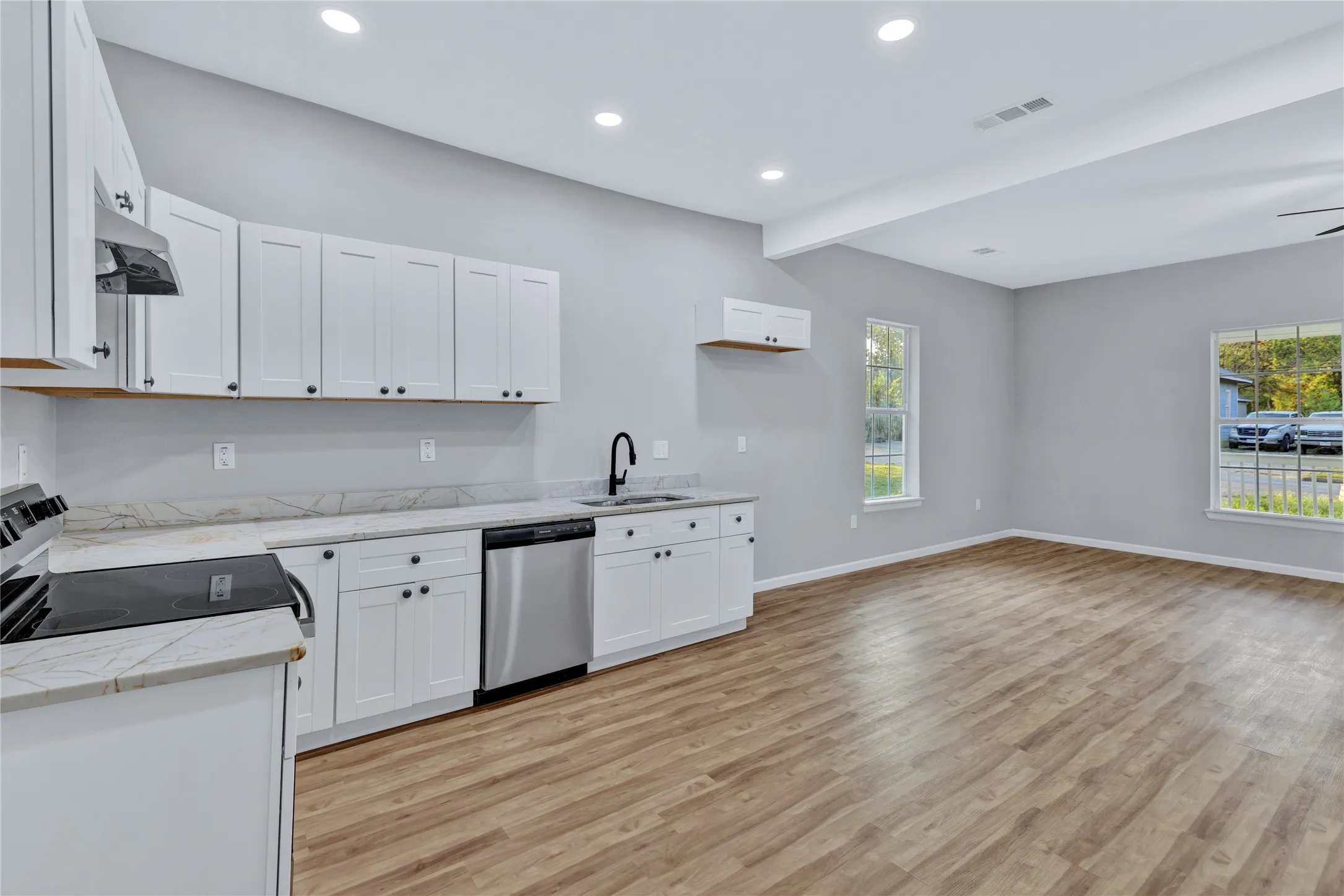 Open-concept living space with wood-finish flooring, white shaker cabinetry, stainless steel appliances, and recessed lighting