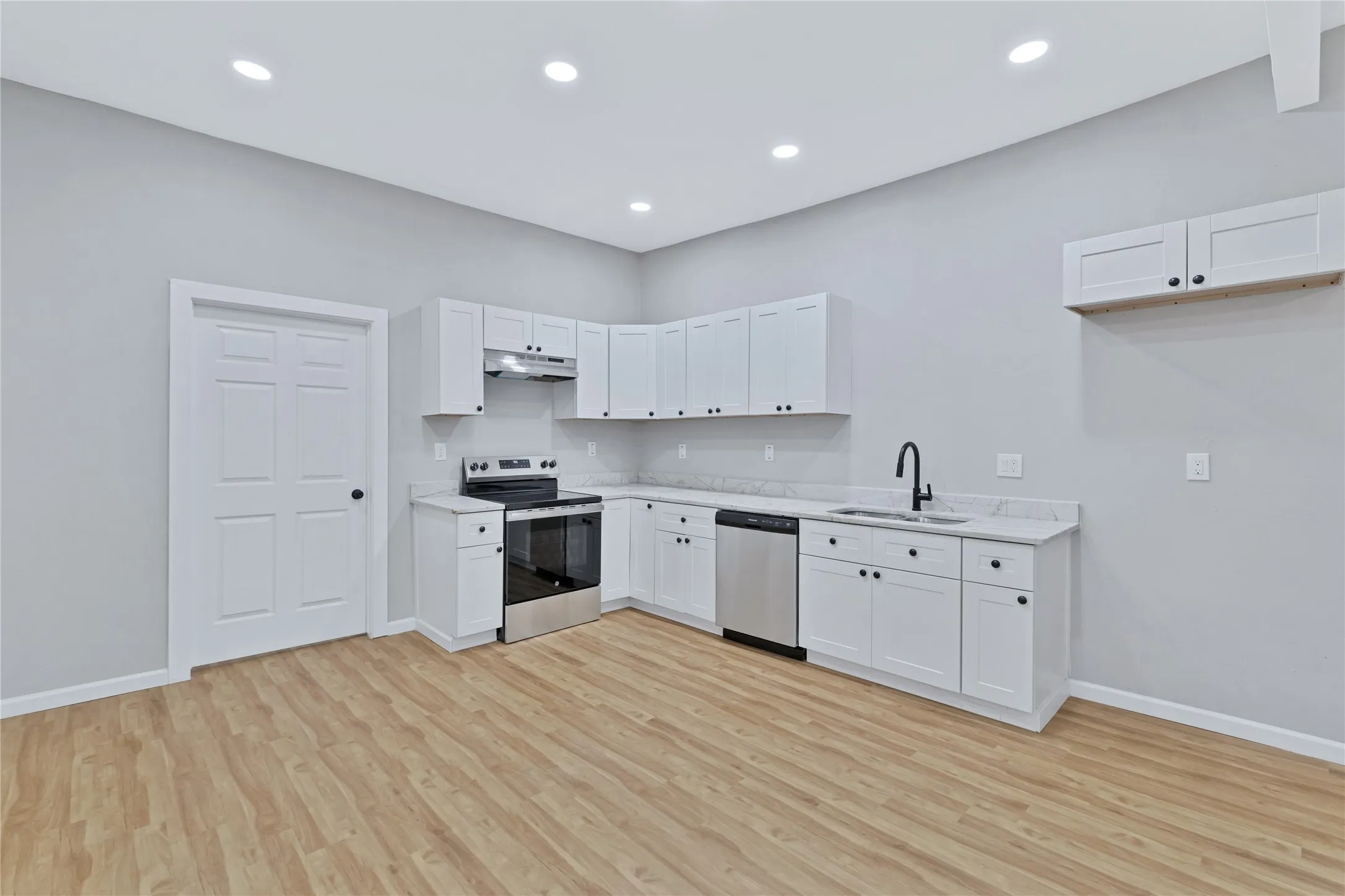 Kitchen featuring white cabinetry, stainless steel appliances, light-toned wood-finish flooring, recessed lighting, and a black-finish faucet