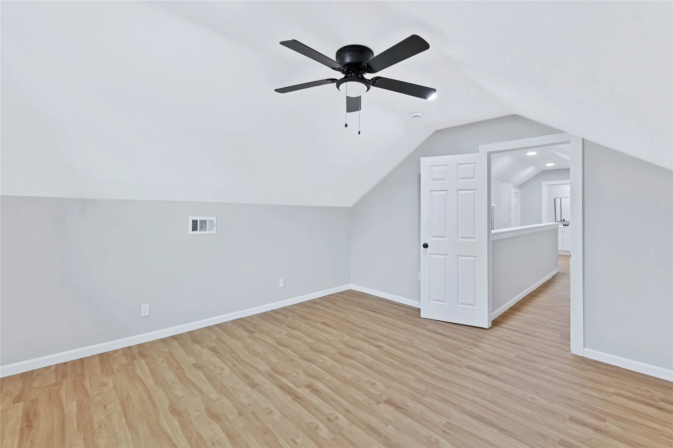 Sloped ceilings, wood-finish flooring, and a ceiling fan with integrated lighting