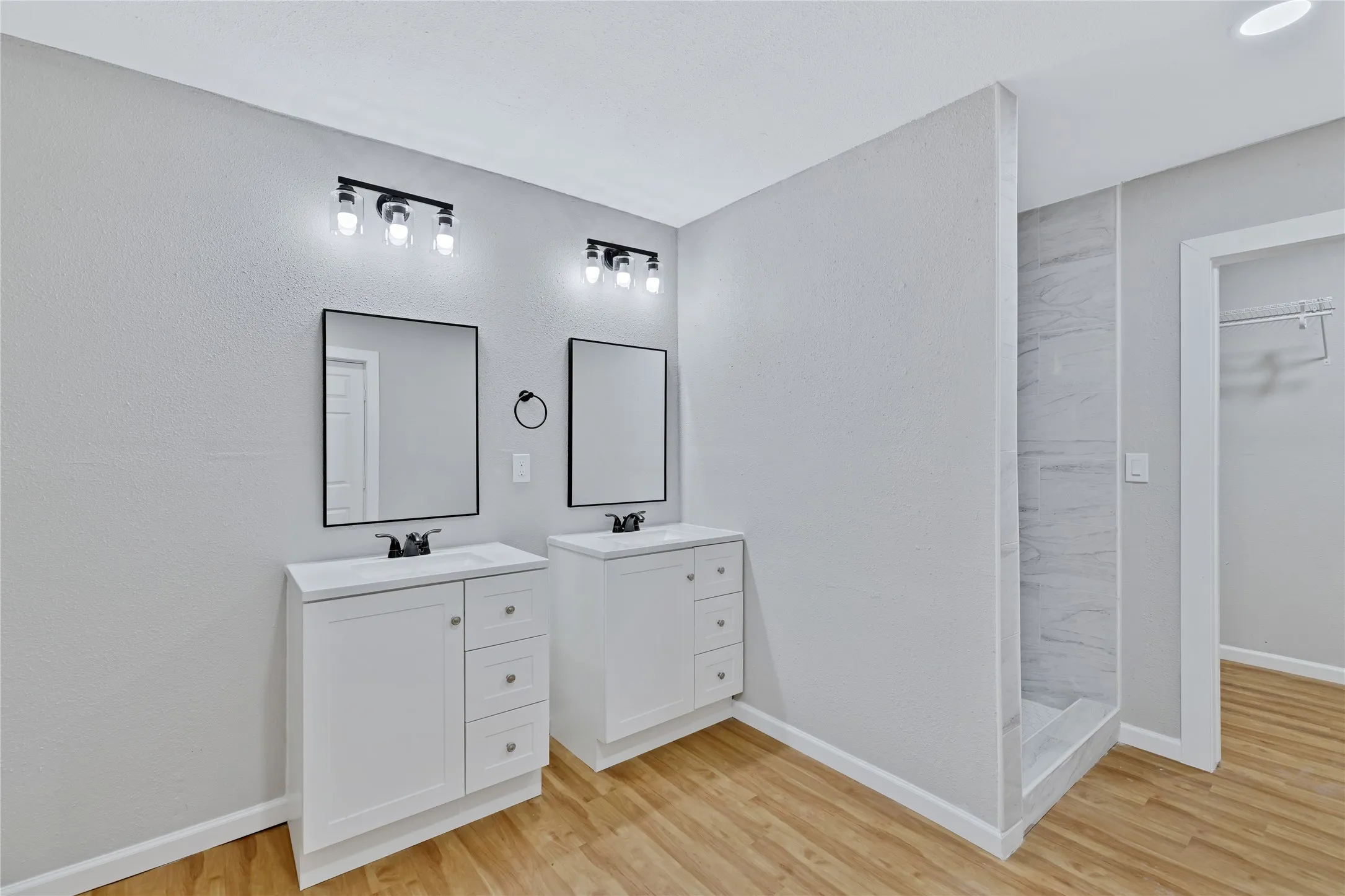 Dual white vanities with integrated sinks, wood-finish flooring, and a tiled shower enclosure