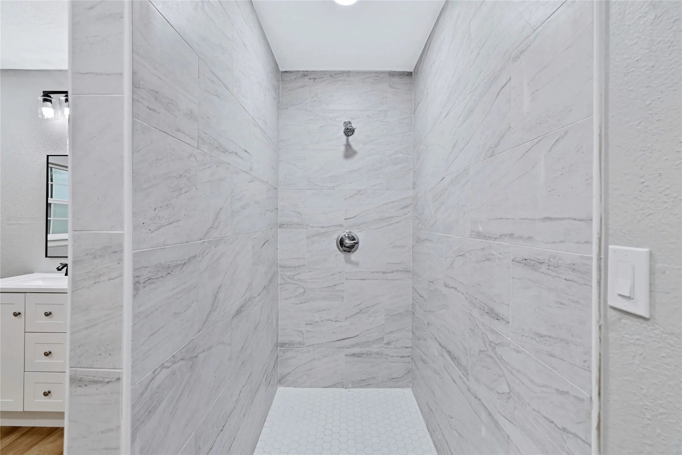 Walk-in shower with large-format tile walls, hexagonal floor tiles, and polished chrome fixtures