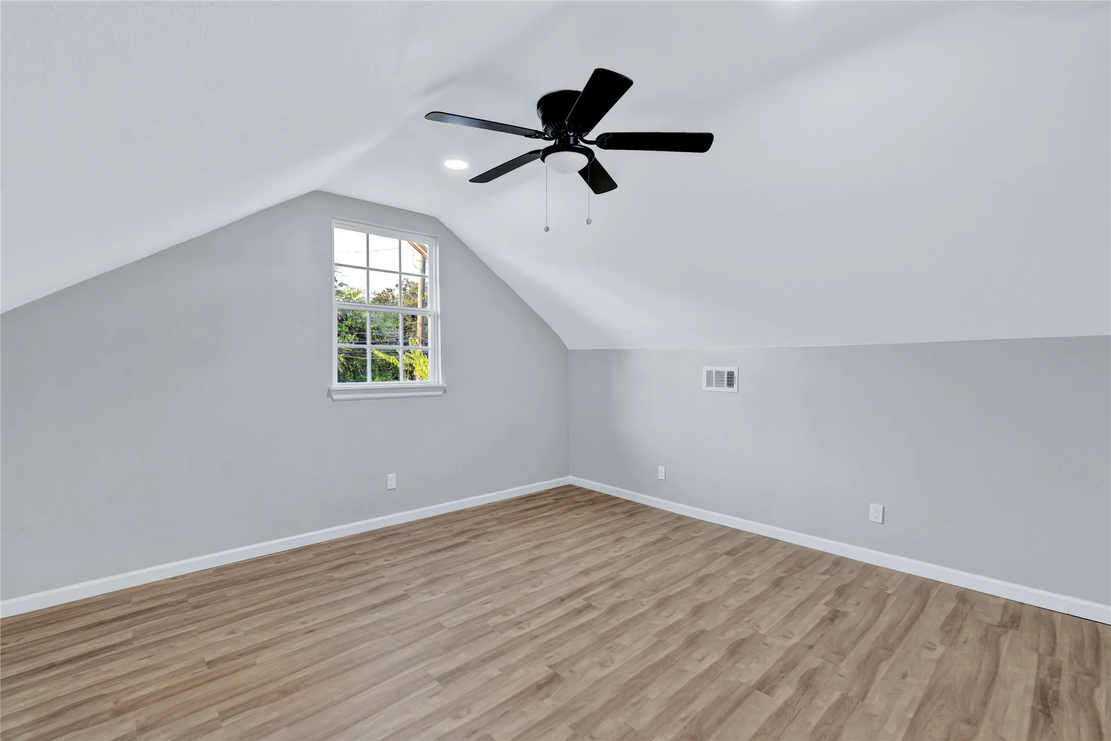 Sloped ceiling room featuring wood-finish flooring, a single-pane window, and a ceiling fan with integrated lighting