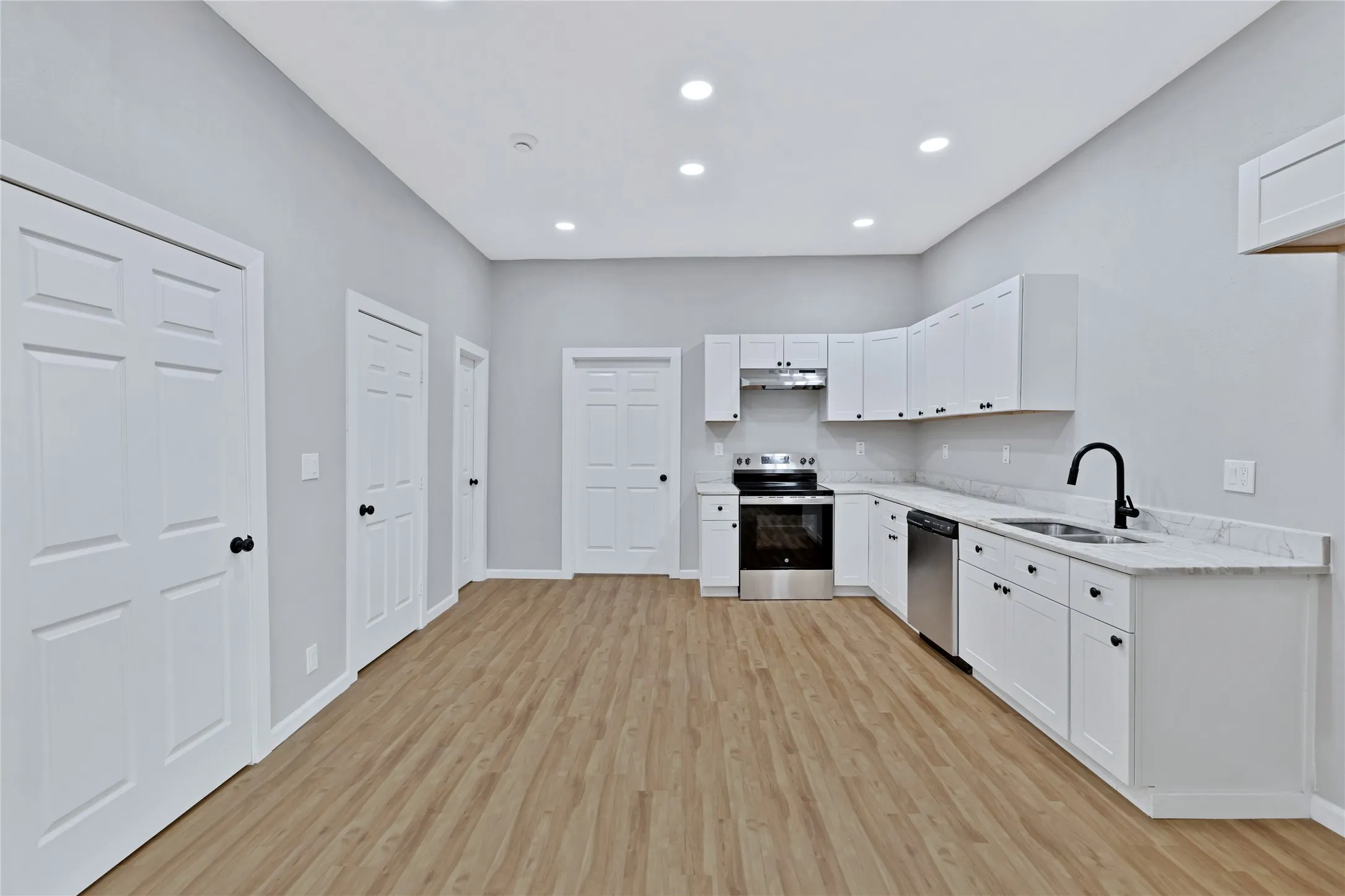 Open-concept kitchen featuring white cabinetry, stone countertops, stainless steel appliances, and wood-finish flooring