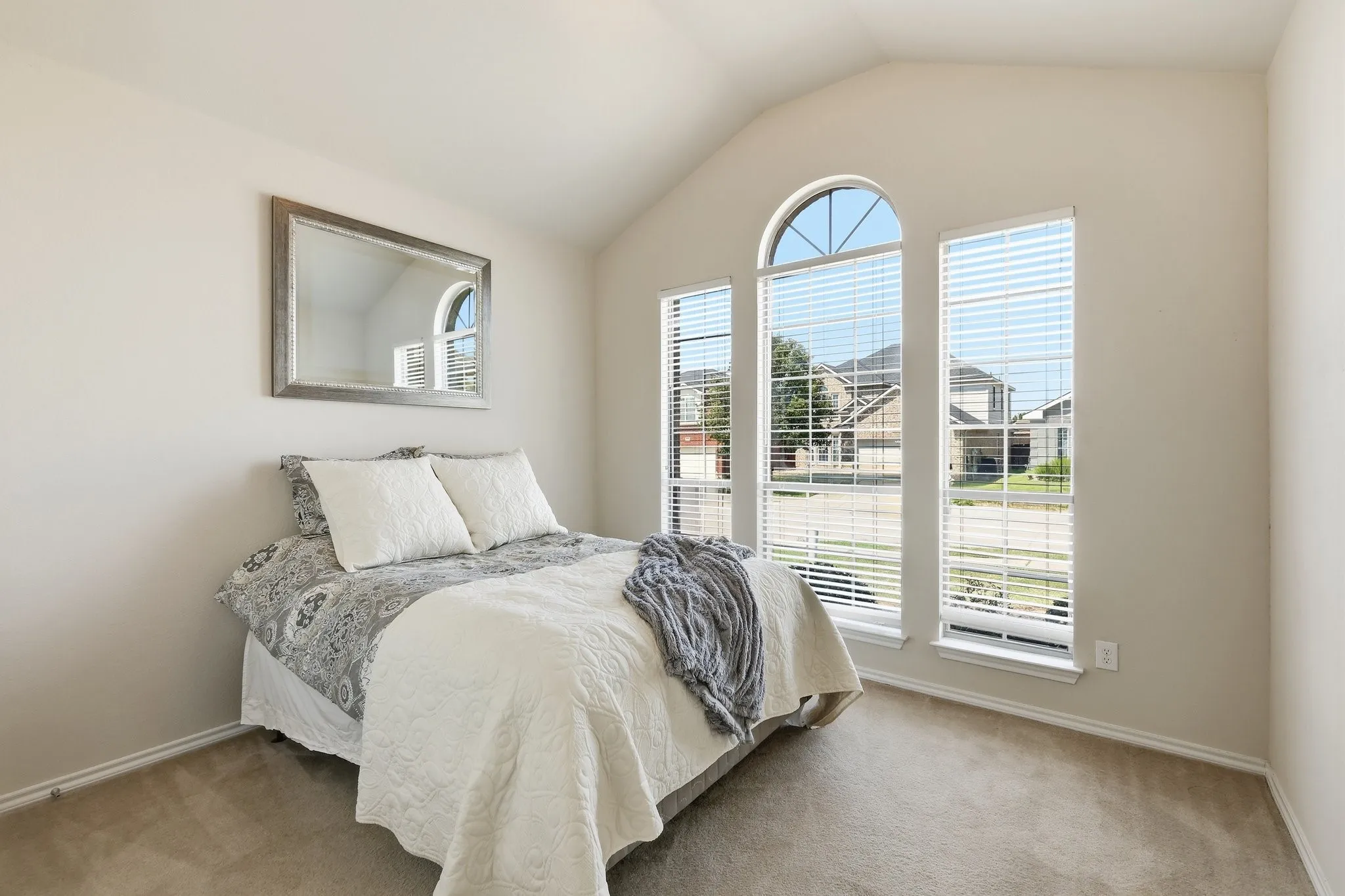 Vaulted ceiling bedroom with light-toned carpet flooring and neutral wall paint