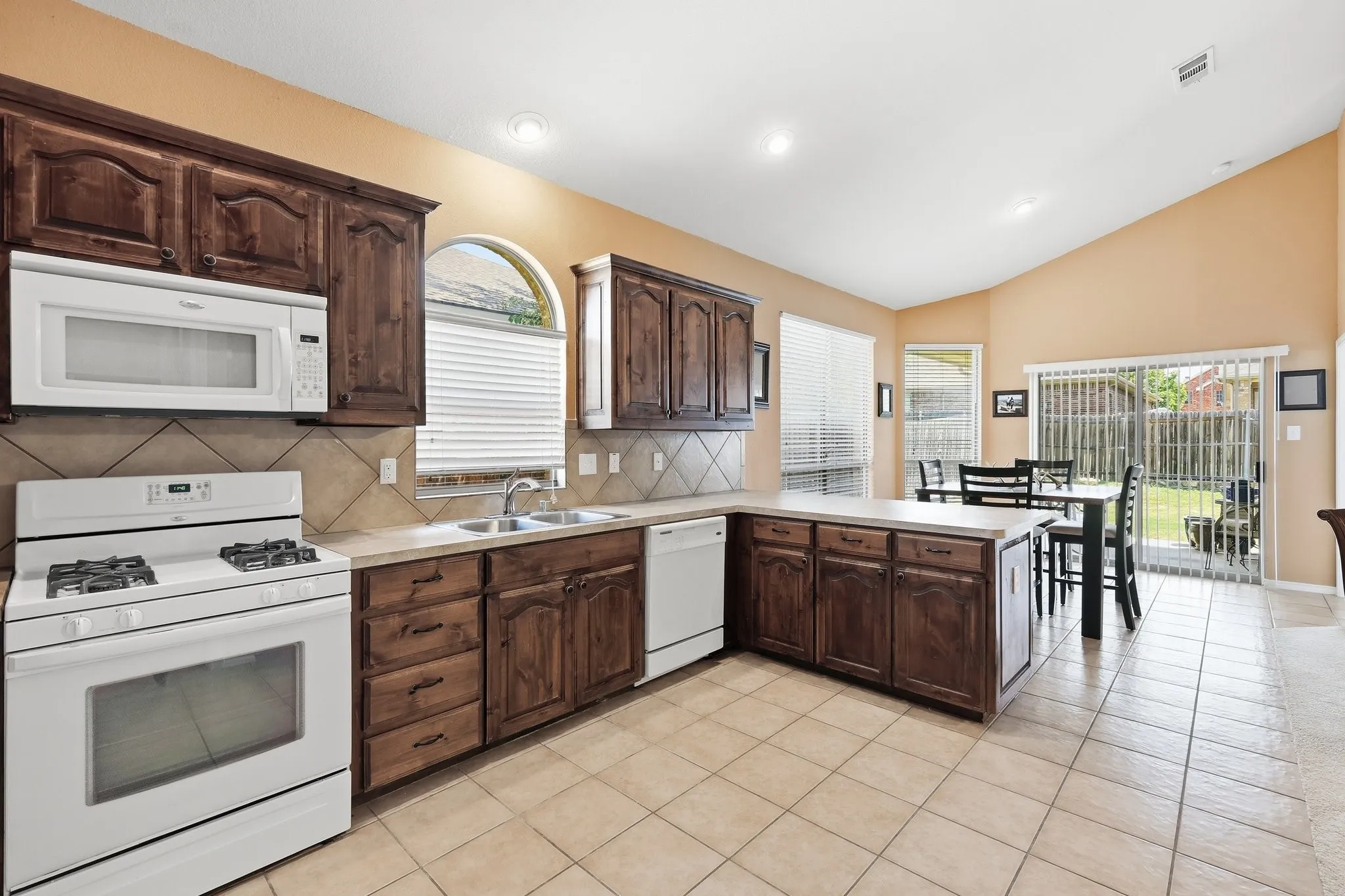 Spacious kitchen featuring dark wood cabinetry, white appliances, tile backsplash, and a breakfast bar
