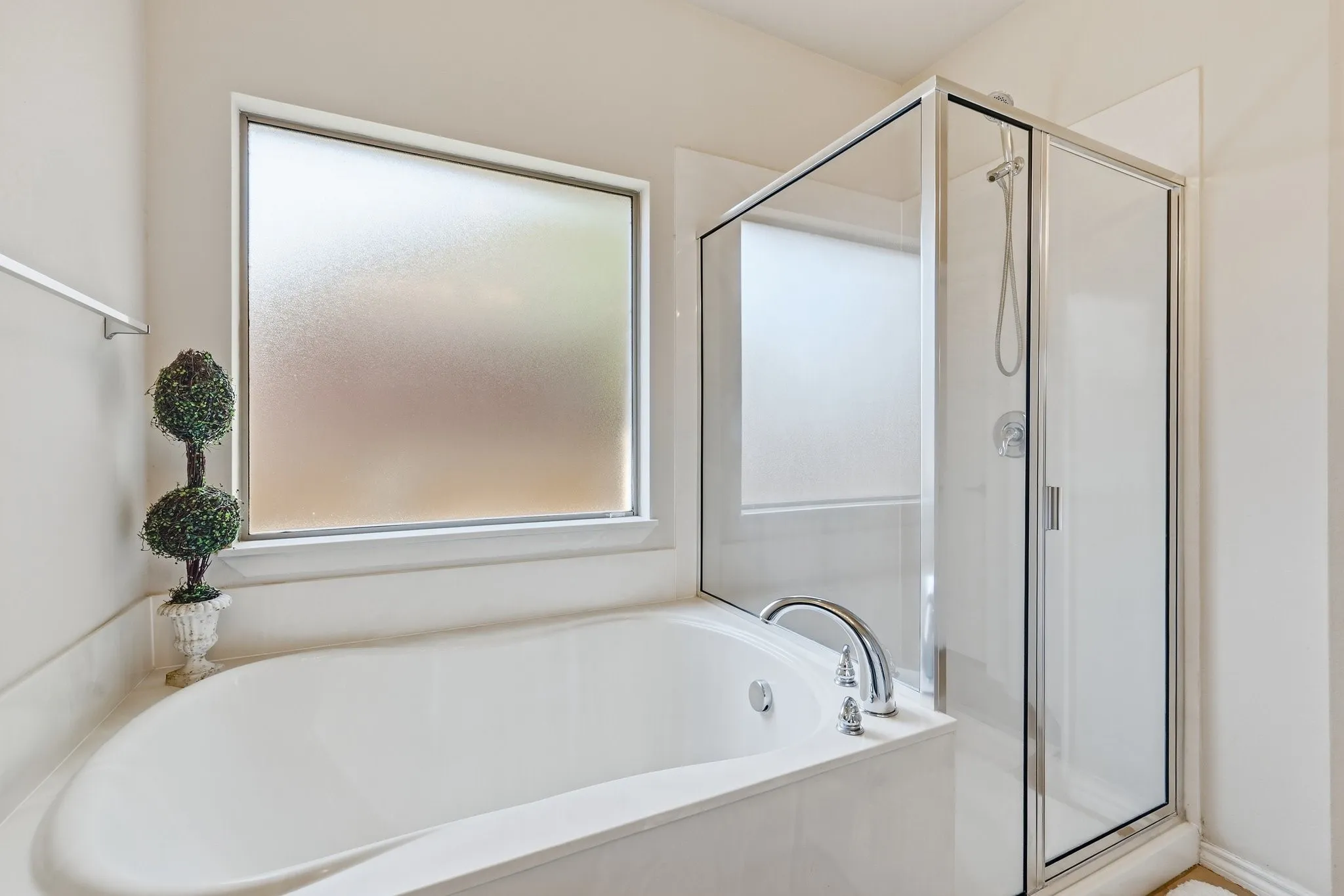 Bathroom featuring a built-in soaking tub with polished chrome fixtures, a frosted privacy window, and a glass-enclosed shower