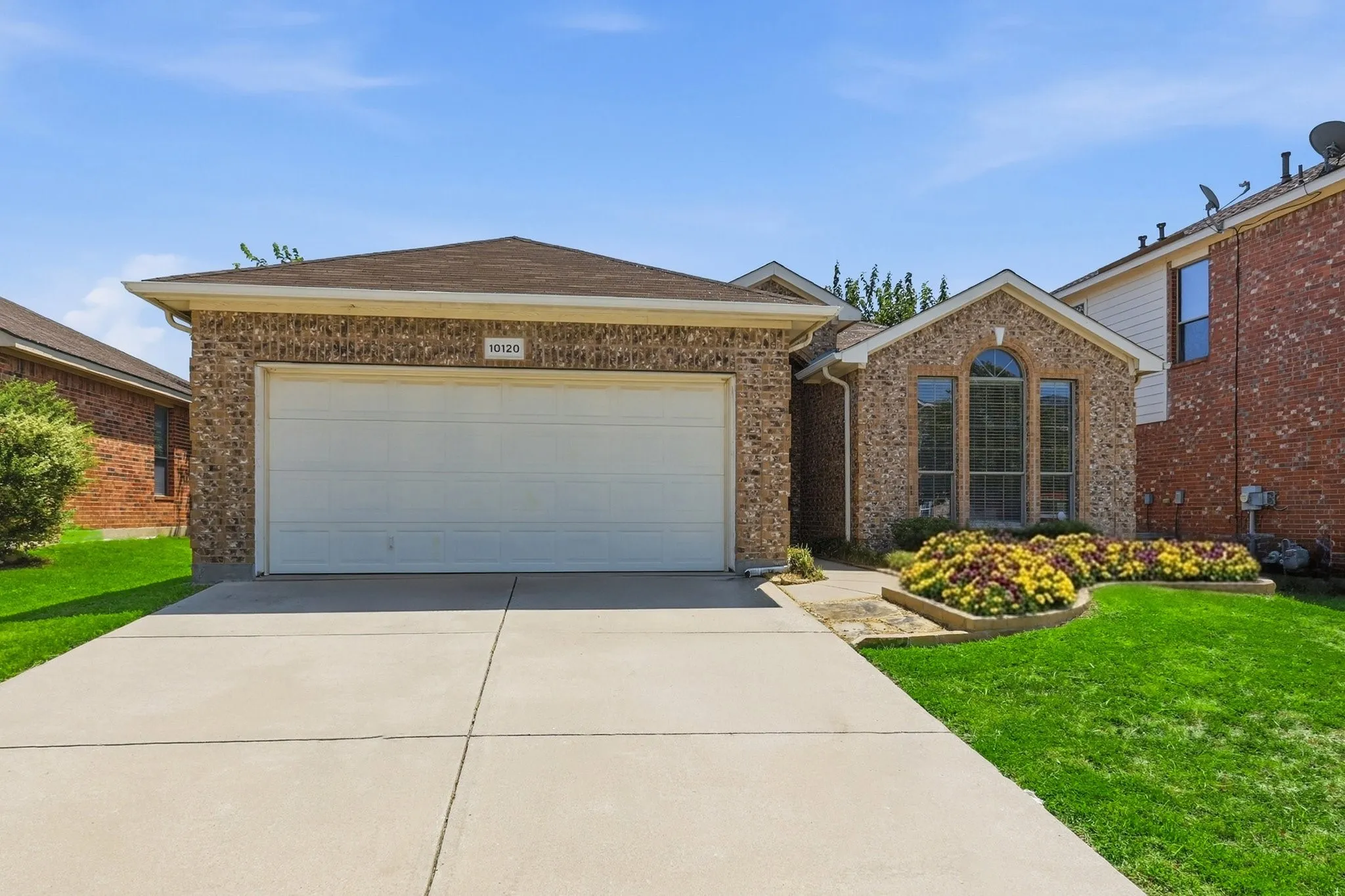Stone-veneer facade featuring an arched window, a two-car garage, concrete driveway, and established landscaping beds