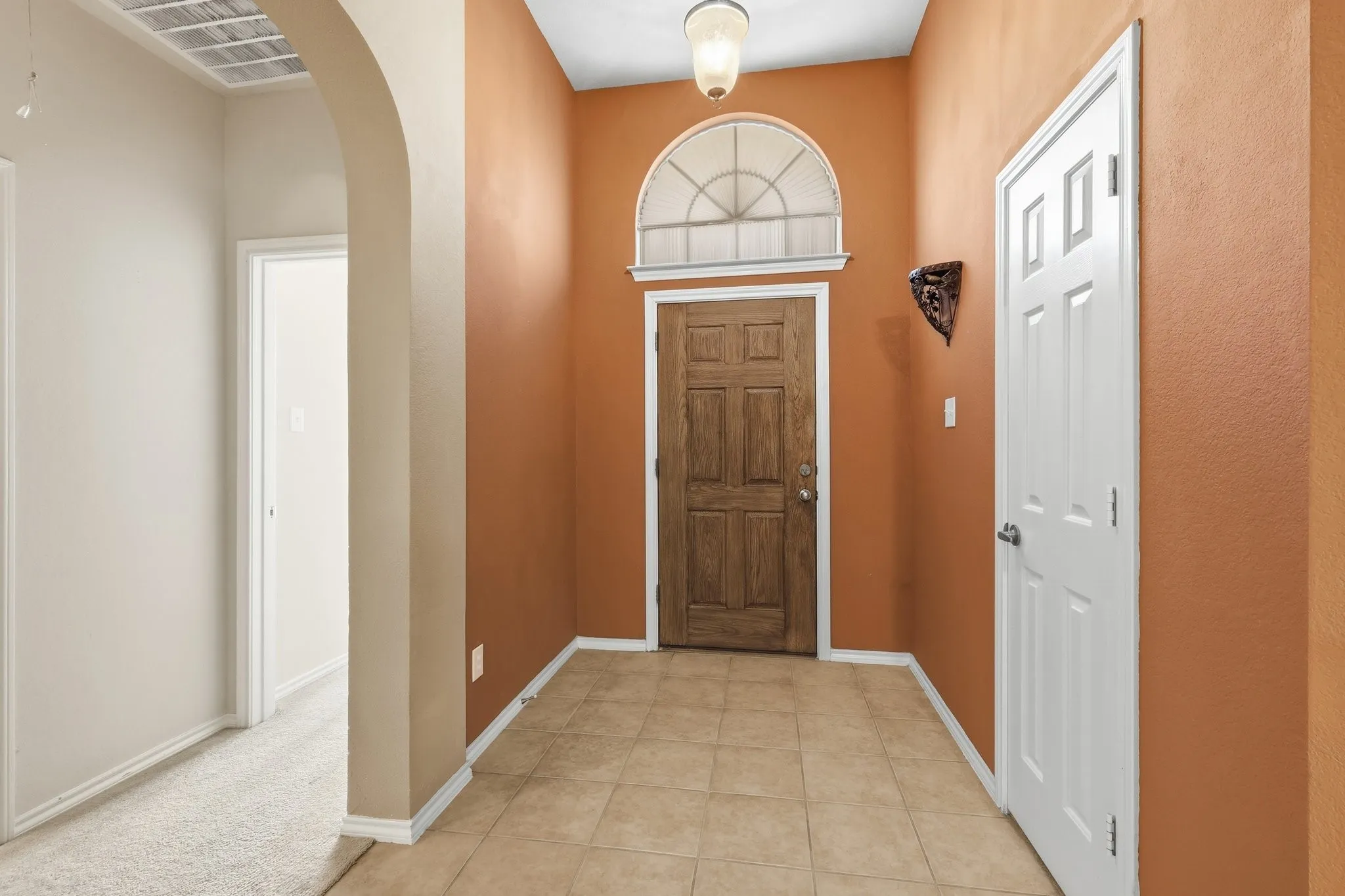 Entryway featuring a panel door with an arched transom window, tiled flooring, an arched doorway, and a built-in wall sconce