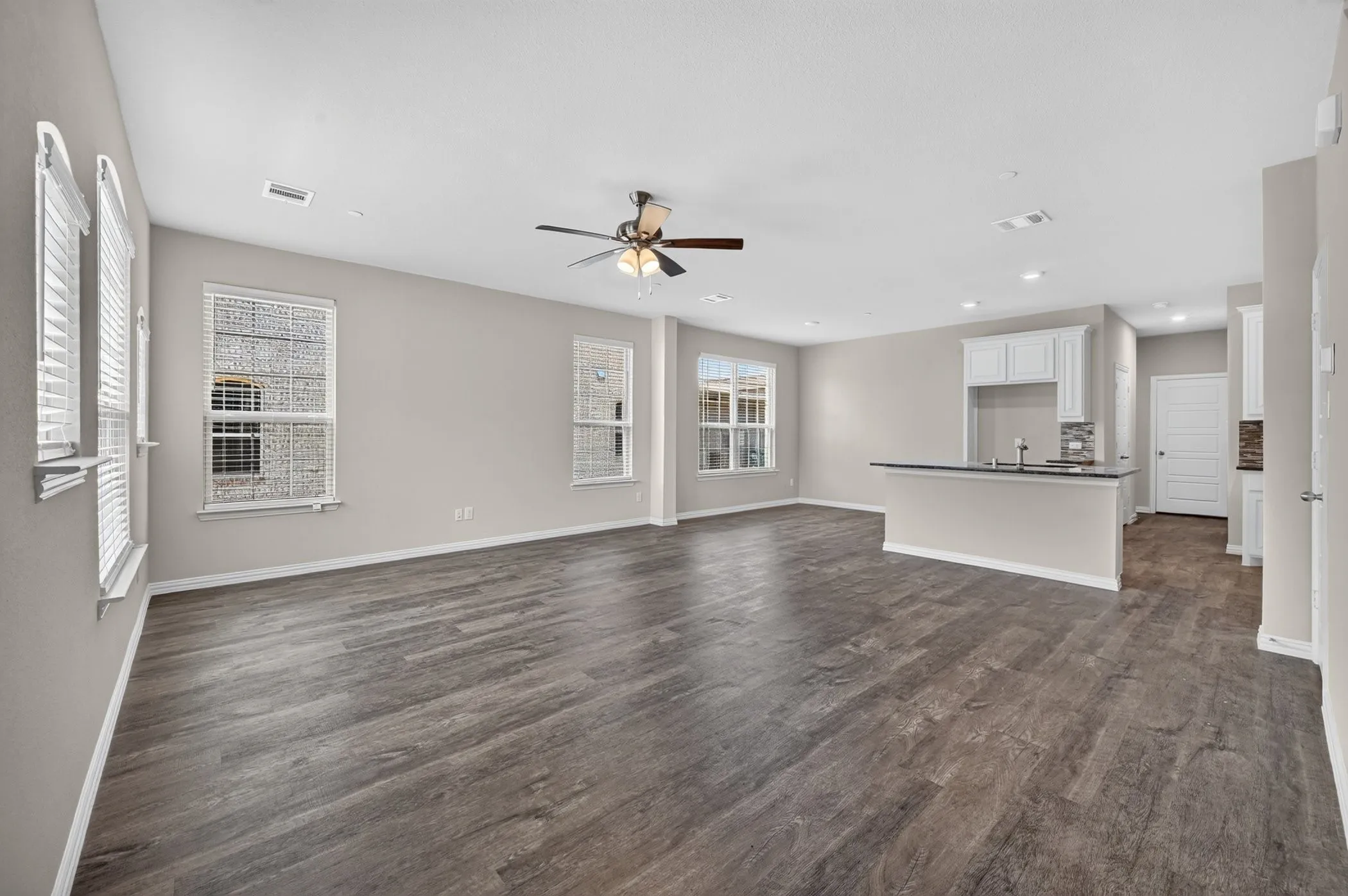 Spacious living area featuring wood-finish flooring, neutral paint tones, multiple windows with blinds, and an integrated ceiling fan