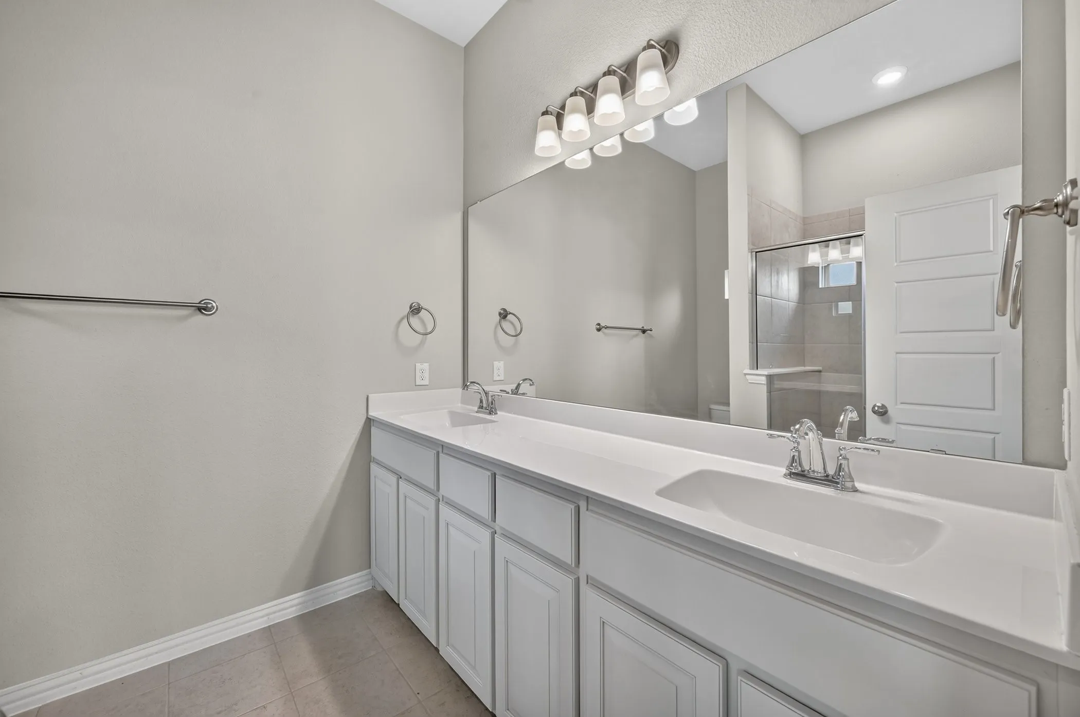 Double vanity with integrated sinks and white cabinetry, featuring chrome fixtures, a full-width mirror, and a multi-bulb light fixture