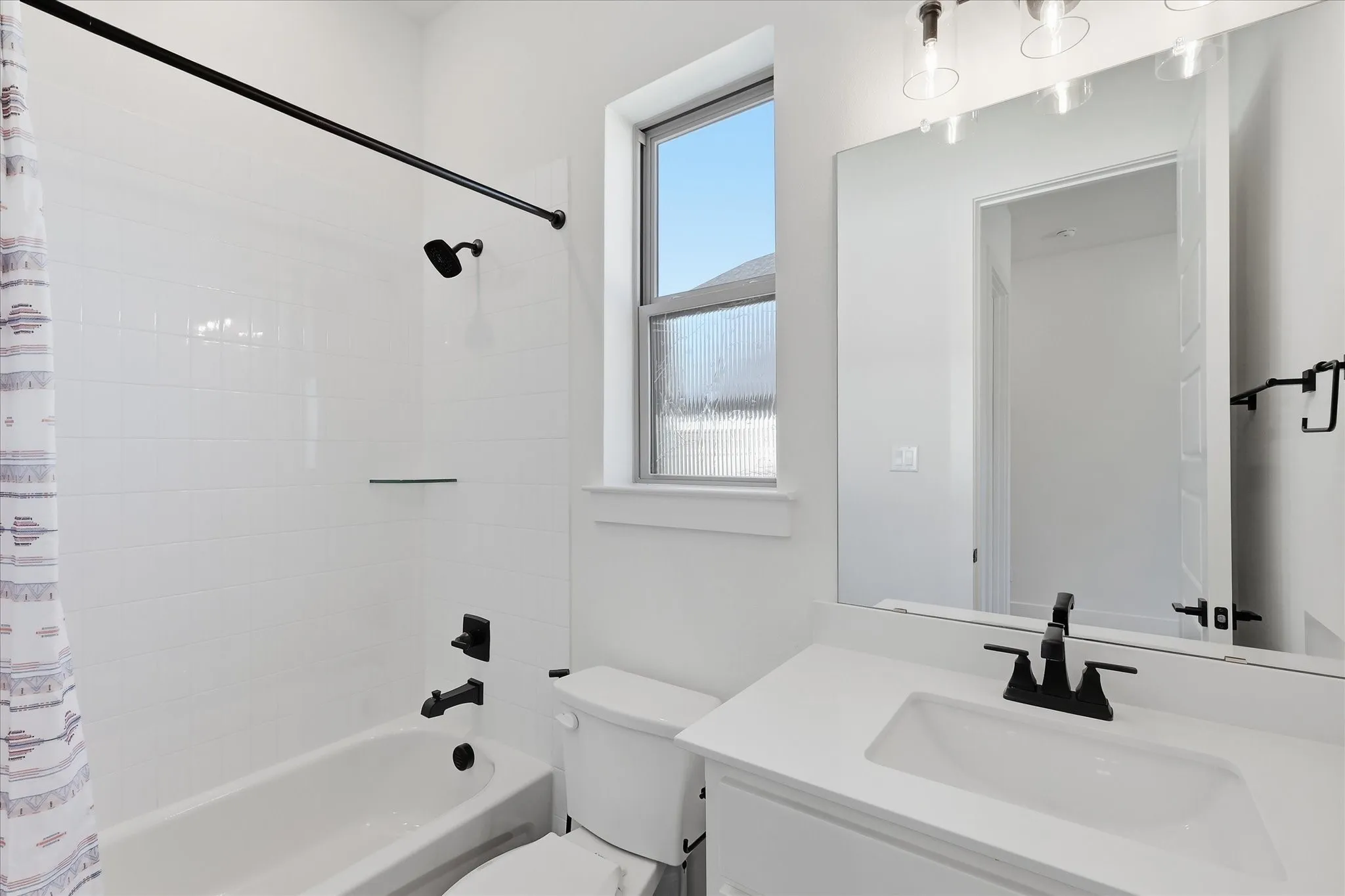 Bright, modern bathroom featuring a spacious vanity with white quartz countertop and matte black hardware, large framed mirror, and a subway tile shower surround with rainfall showerhead