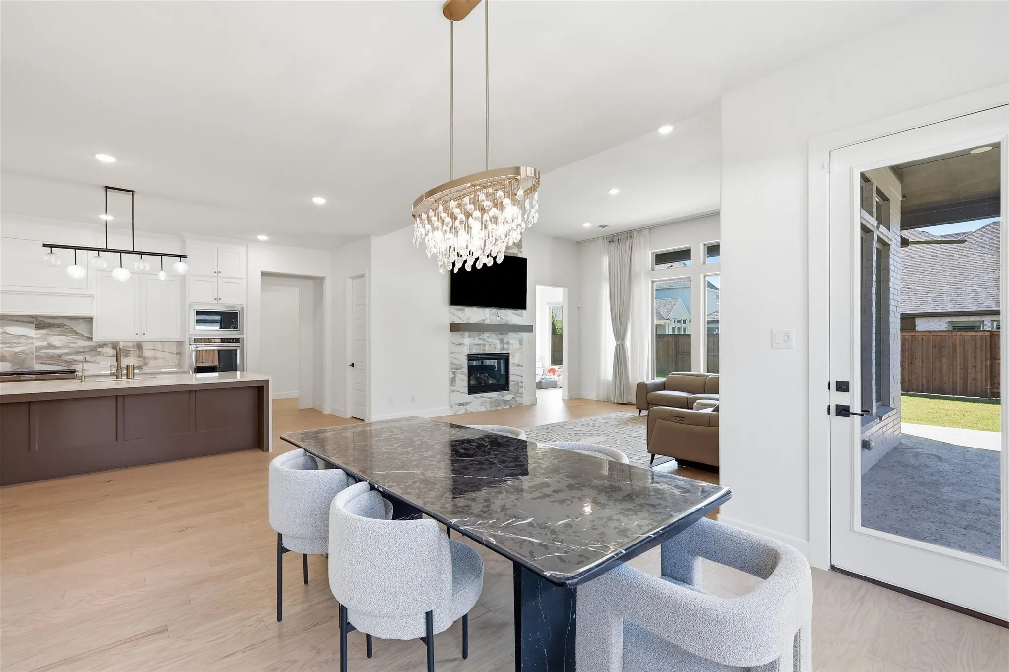 Open-concept kitchen and dining area featuring a large quartz-topped island with seating for four, stainless steel built-in appliances, white cabinetry, and wood-finish flooring throughout