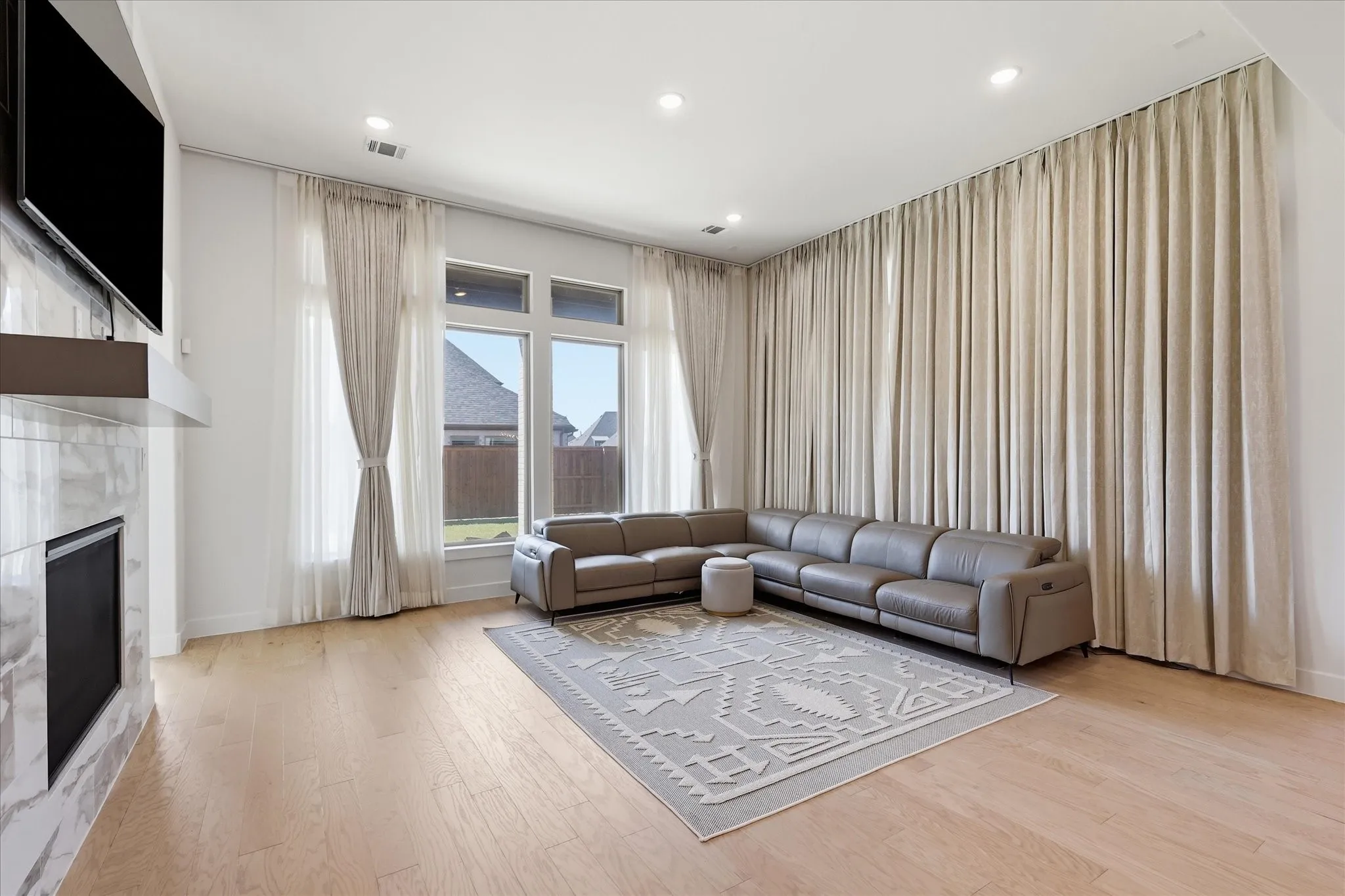 Spacious living room showcasing soaring ceilings, recessed lighting, and floor-to-ceiling drapery framing expansive windows and glass doors