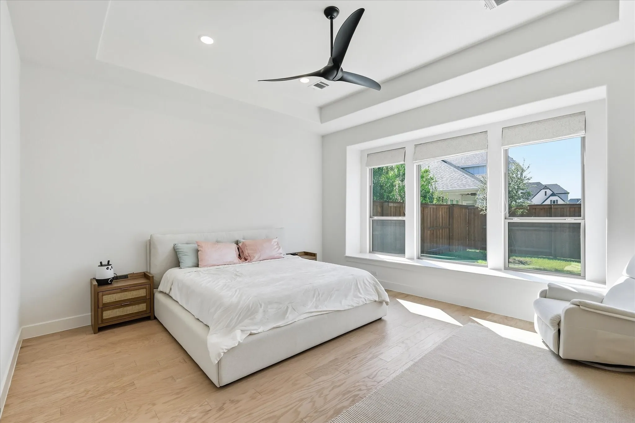 Tray ceiling with recessed lighting, light wood-finish flooring, three large windows, window seat, and a ceiling fan