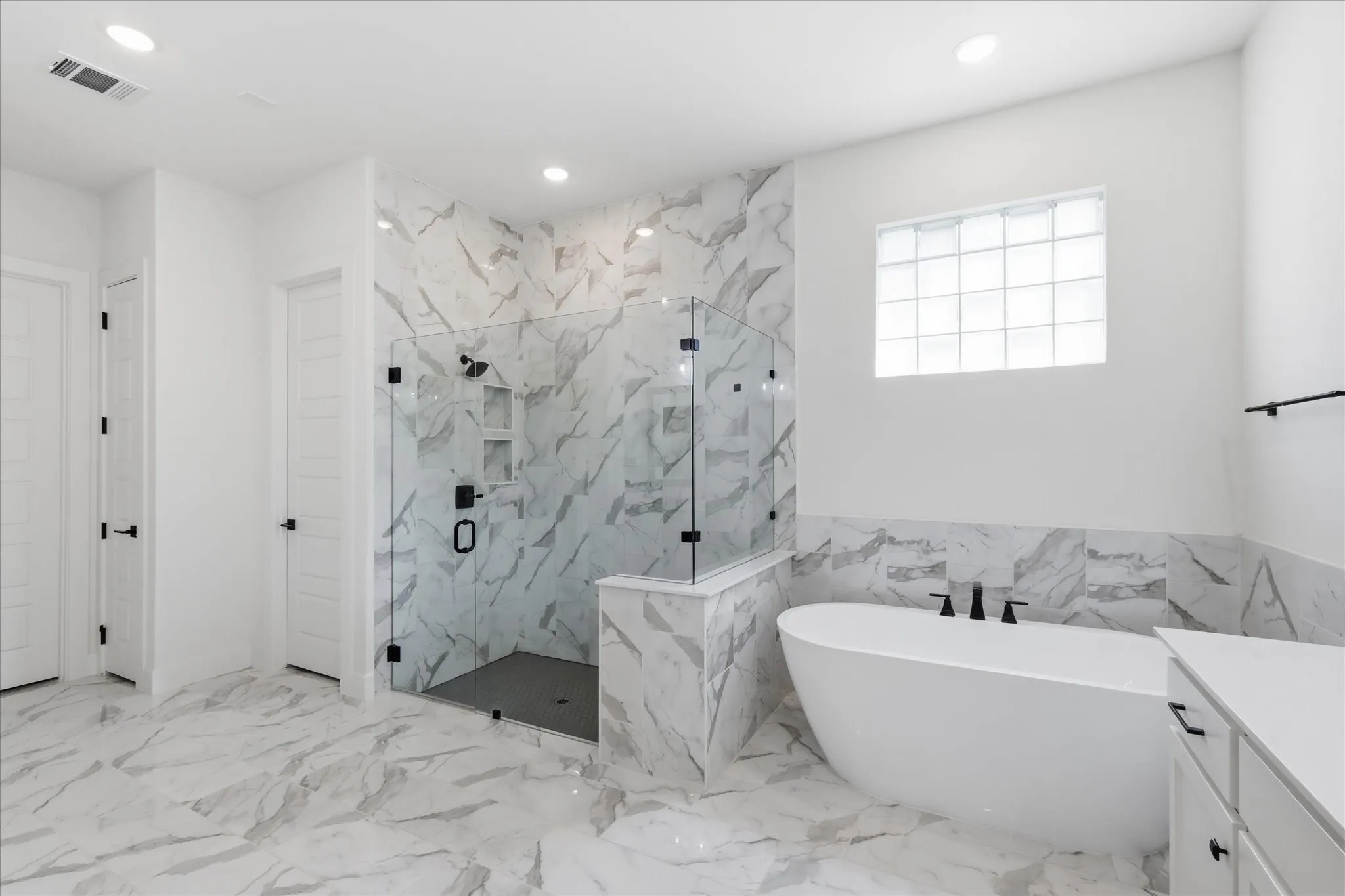 Spacious bathroom featuring large format marble-look tile flooring and accent walls
