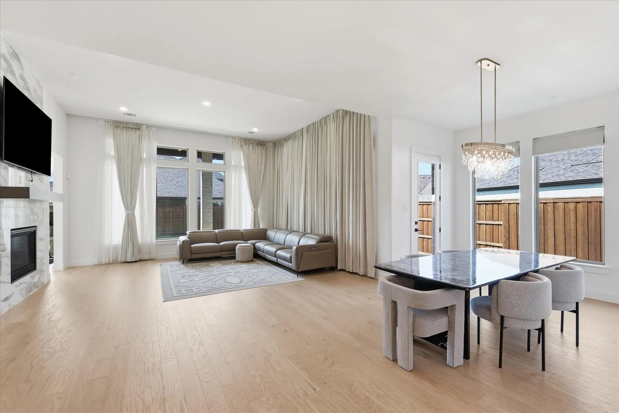 Open-concept living space featuring light wood-finish flooring throughout, a linear dining table with upholstered seating, and a sectional sofa arrangement