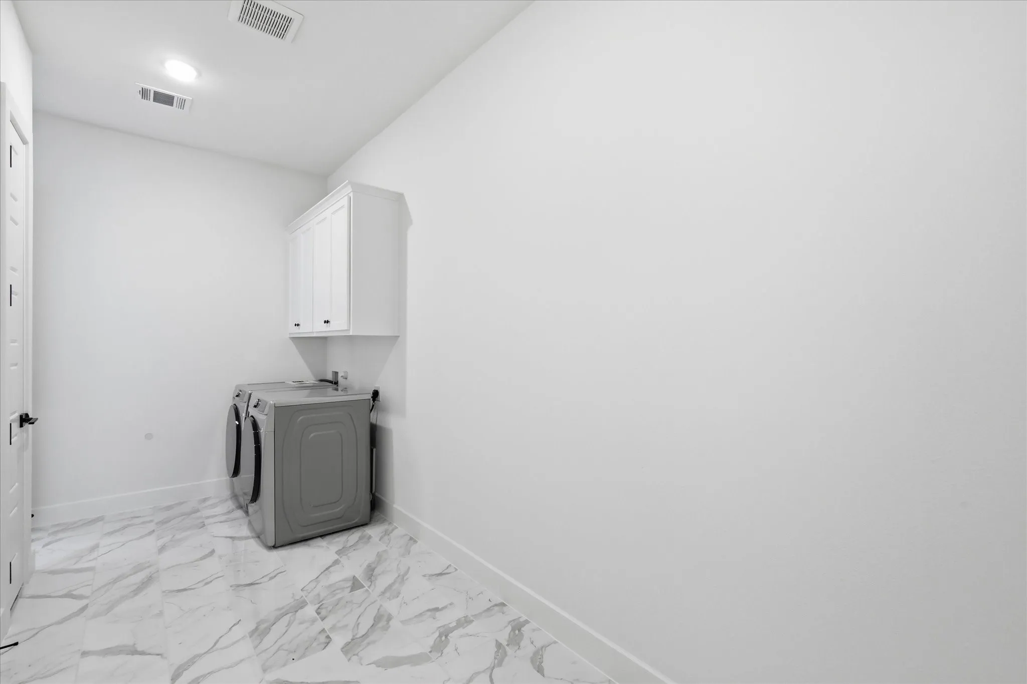 Utility room featuring polished marble-finish flooring, white cabinetry with upper storage, stainless steel sink with wall-mounted faucet, and recessed ceiling lighting
