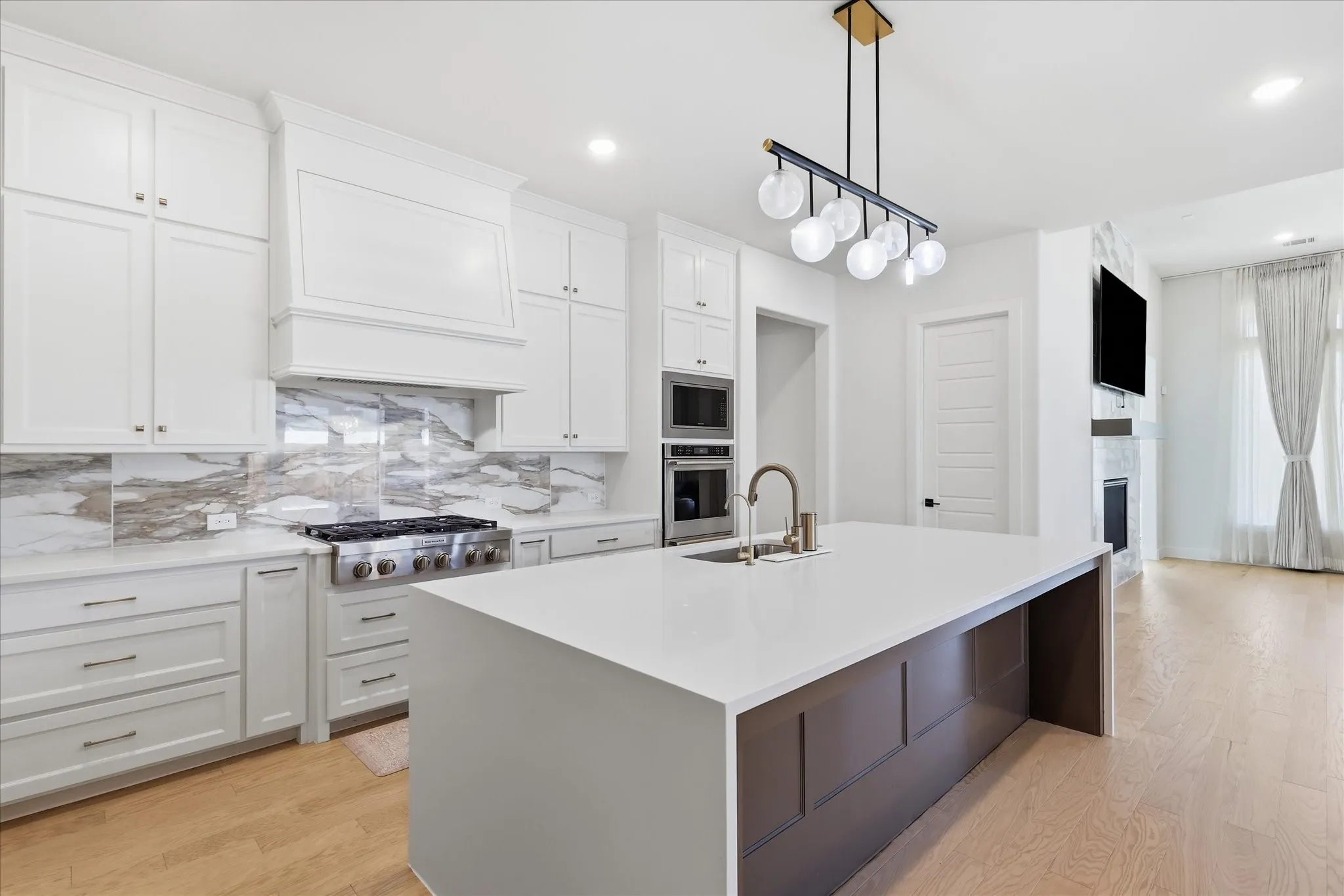 Kitchen featuring white shaker cabinetry, stainless steel range, built-in double oven, waterfall island with sink, and light wood-finish flooring