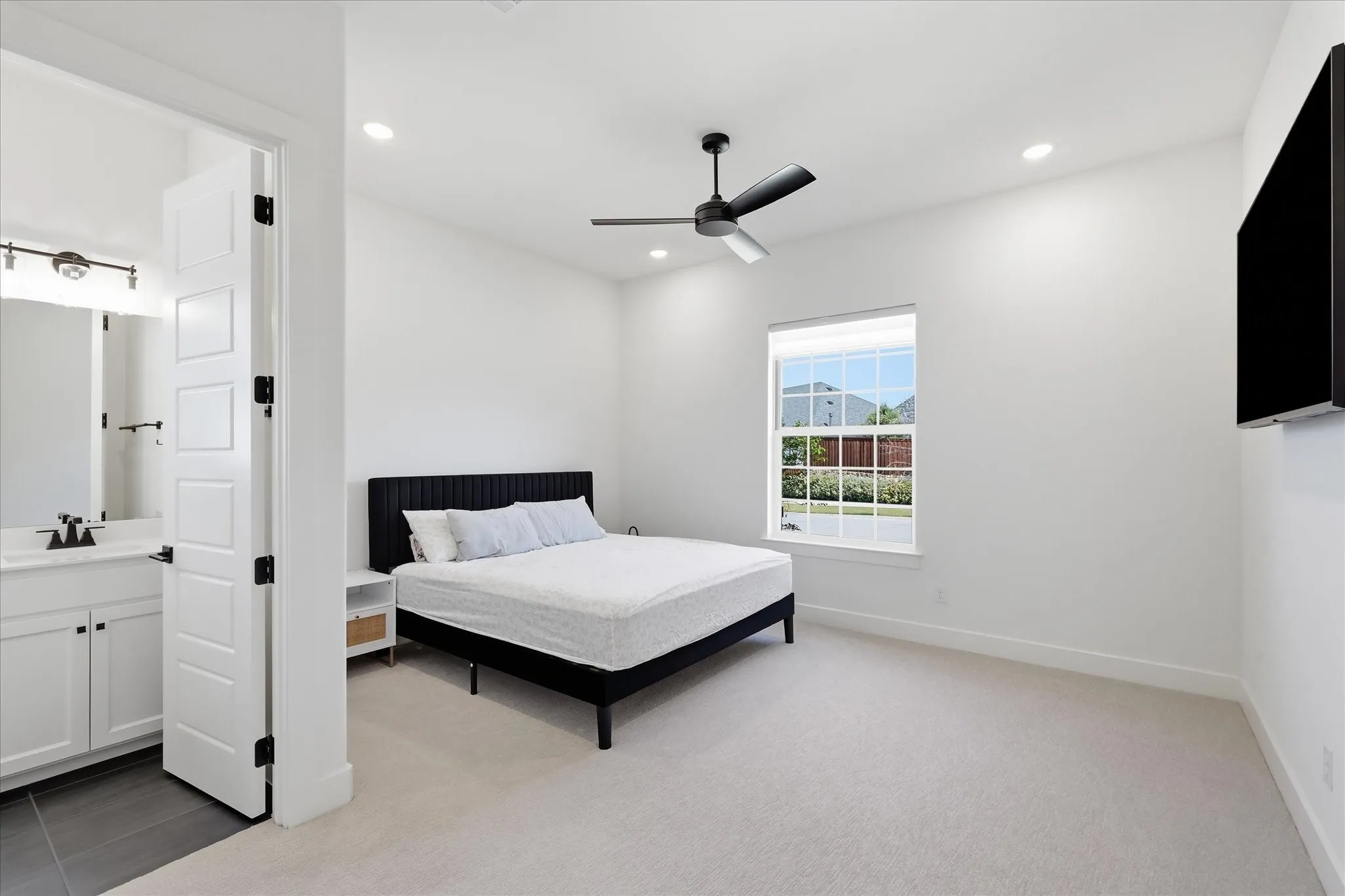 Spacious primary bedroom featuring a black platform bed frame, soft neutral carpeting, and recessed ceiling lighting