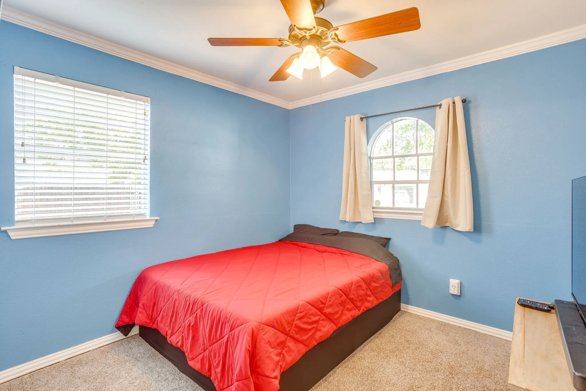 Bright secondary bedroom featuring soft blue walls, carpeted flooring, ceiling fan with integrated lighting, and dual windows with natural light