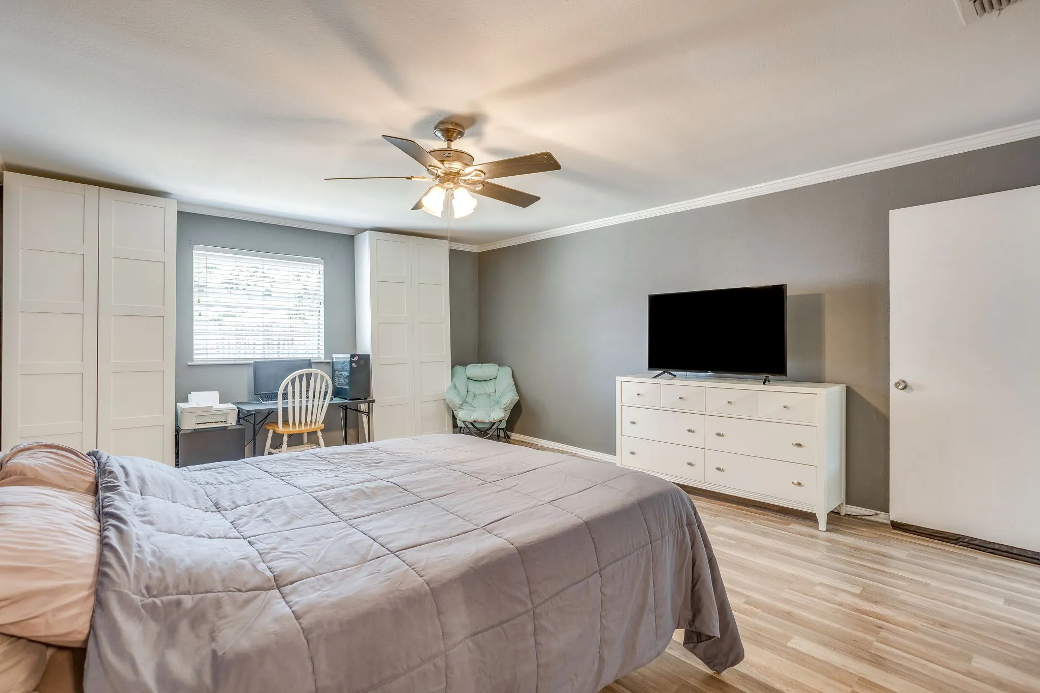 Spacious primary bedroom featuring wood-finish flooring, ceiling fan with integrated lighting, and ample natural light from multiple windows