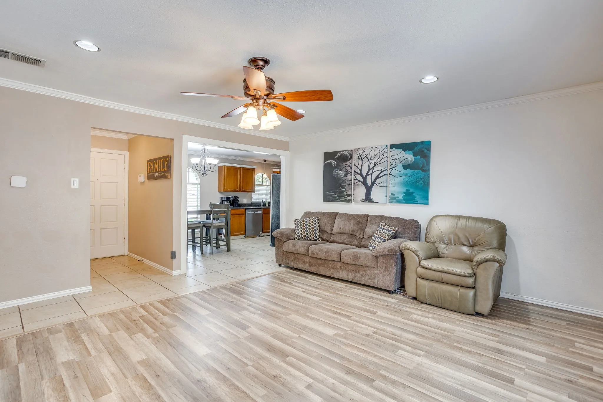 Spacious living area showcasing wood-finish flooring throughout, recessed ceiling lighting, and a ceiling fan with bronze finish