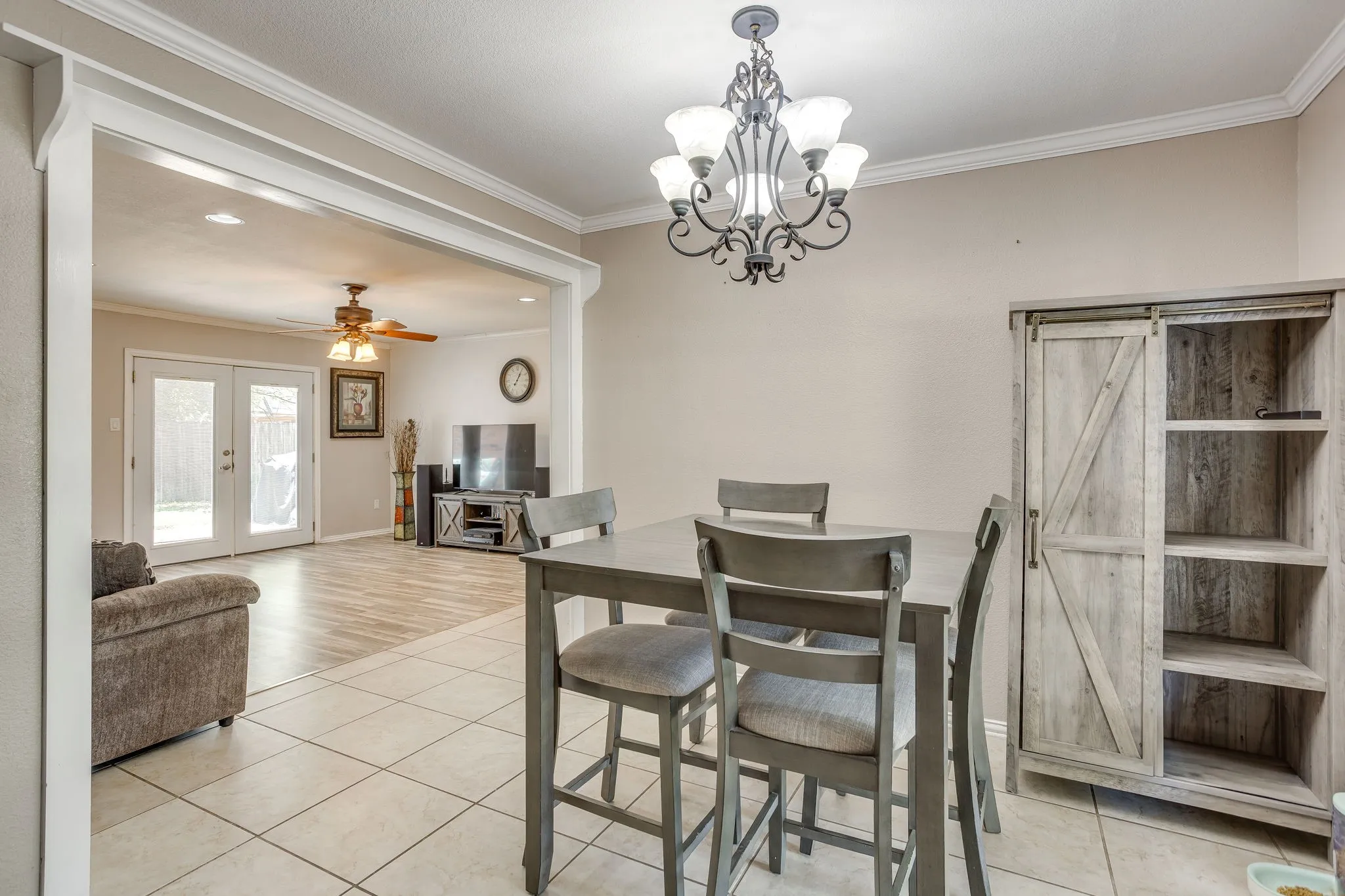 Open dining area with a wood-finish table and upholstered chairs, ceramic tile flooring, and a decorative chandelier overhead