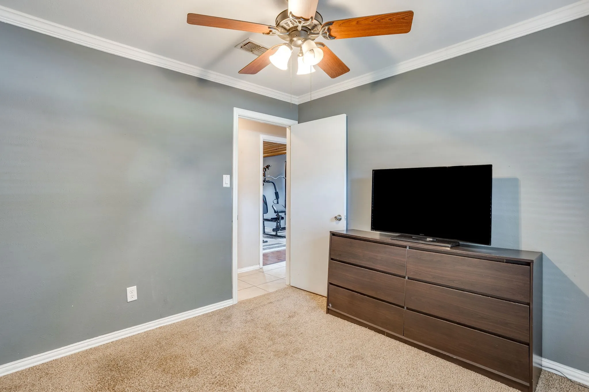 Carpeted interior space featuring a ceiling fan with light kit, crown molding, and baseboards