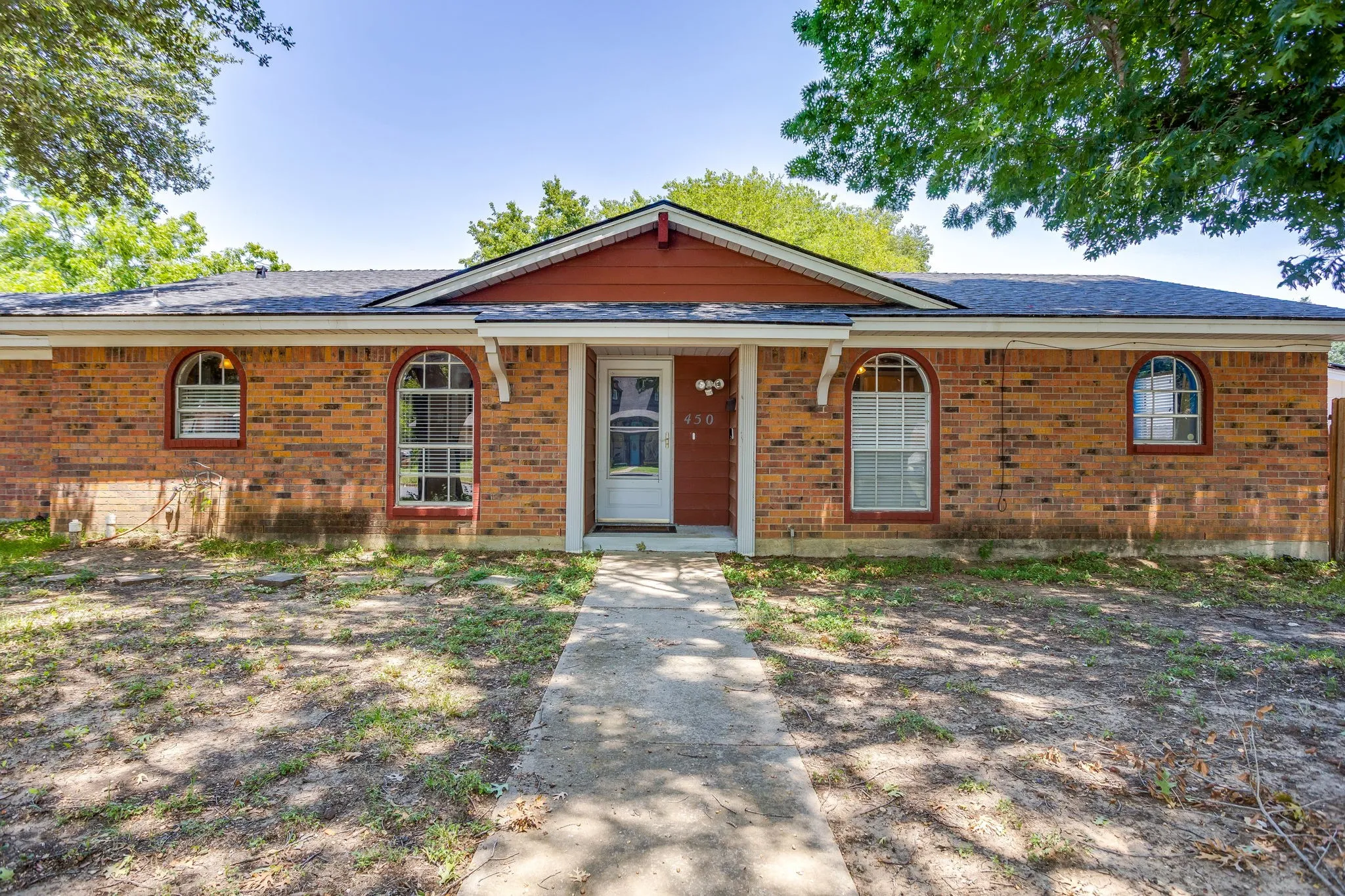 Charming brick ranch home featuring a welcoming front facade with arched transom windows, a covered entry portico with red door accent, and mature landscaping framing the property
