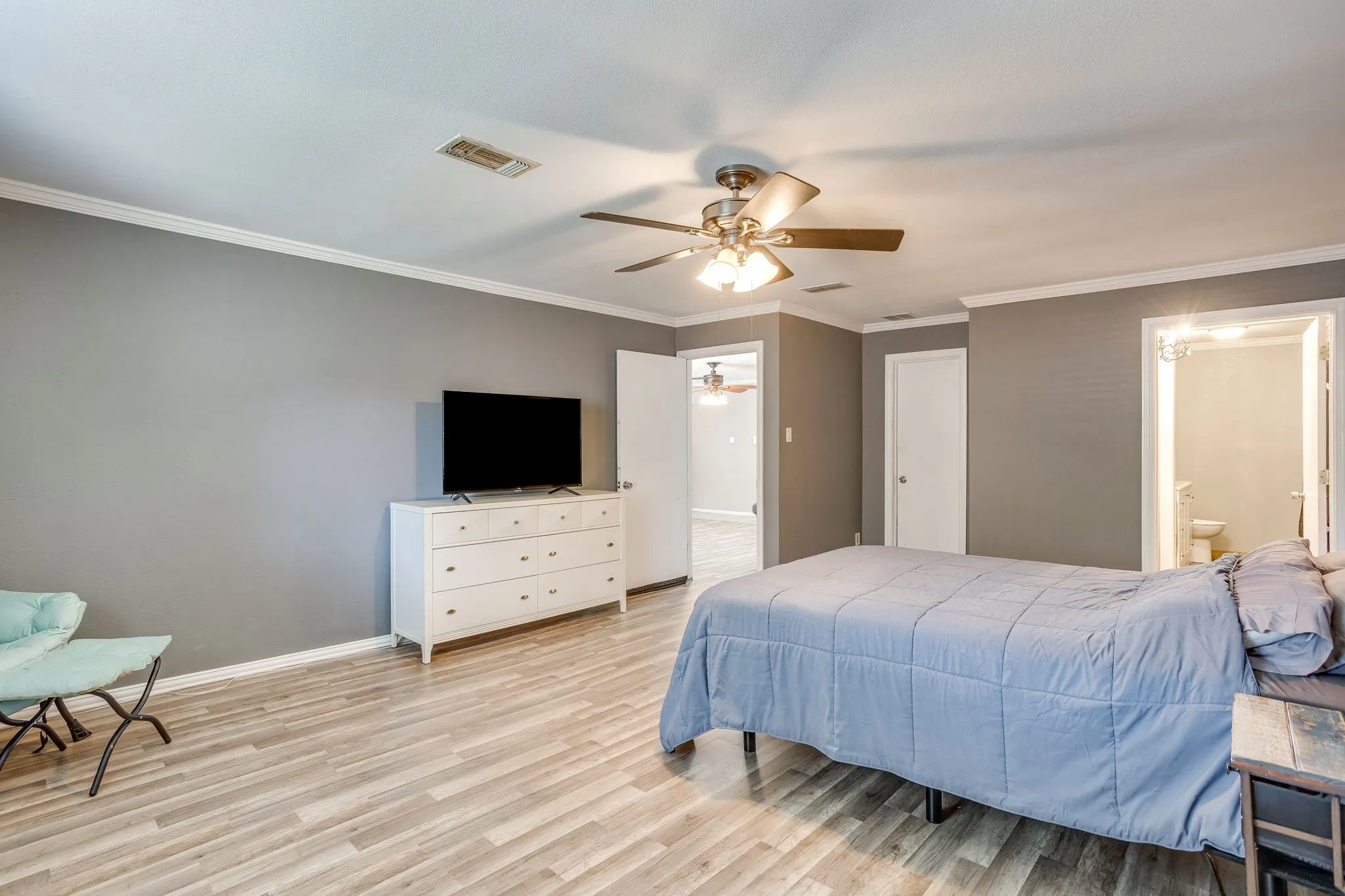 Spacious primary bedroom featuring wood-finish flooring, ceiling fan with integrated lighting, and ample natural light from multiple windows