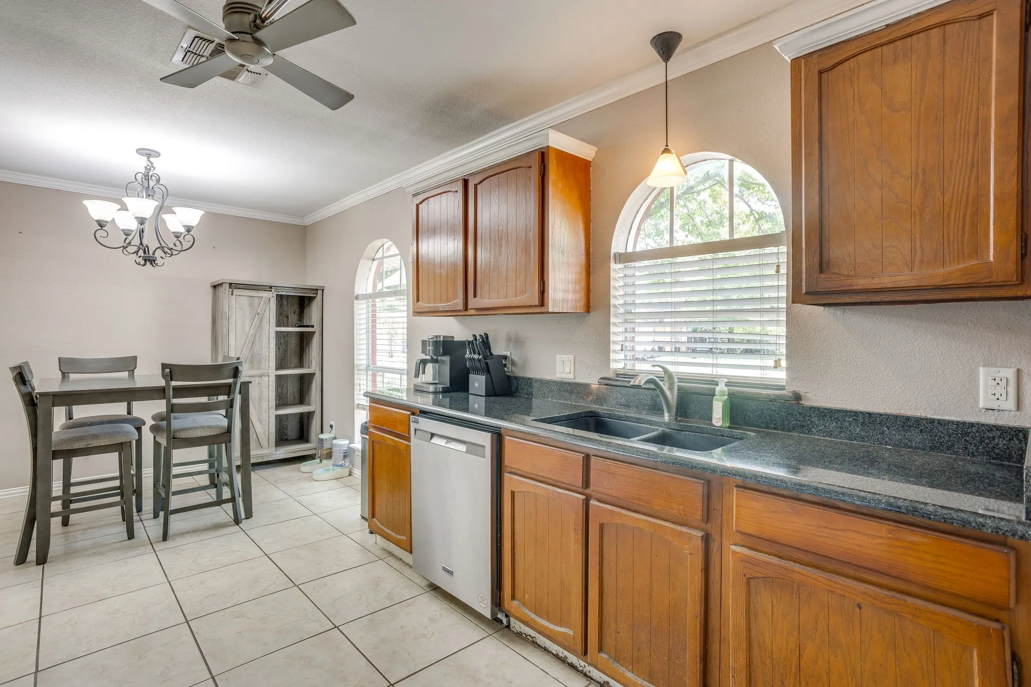Spacious kitchen featuring warm wood cabinetry, dark stone countertops, stainless steel appliances, and abundant natural light from arched windows