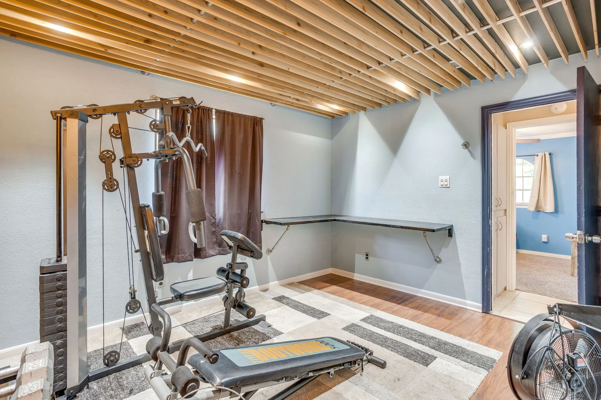 Room featuring a wood-slat ceiling with recessed lighting, light blue wall paint, wood-finish flooring, and a built-in corner desk