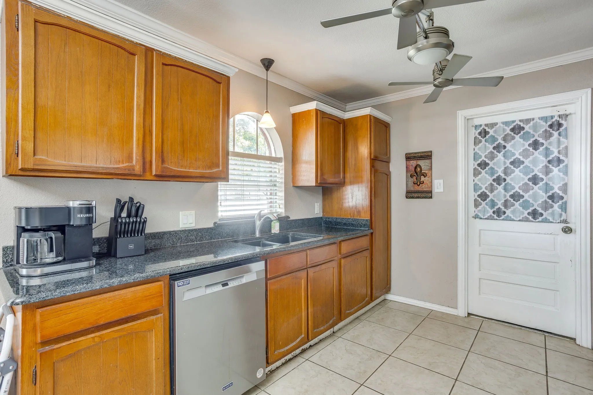 Kitchen featuring wood-finish cabinetry, dark speckled countertops, and a stainless steel dishwasher