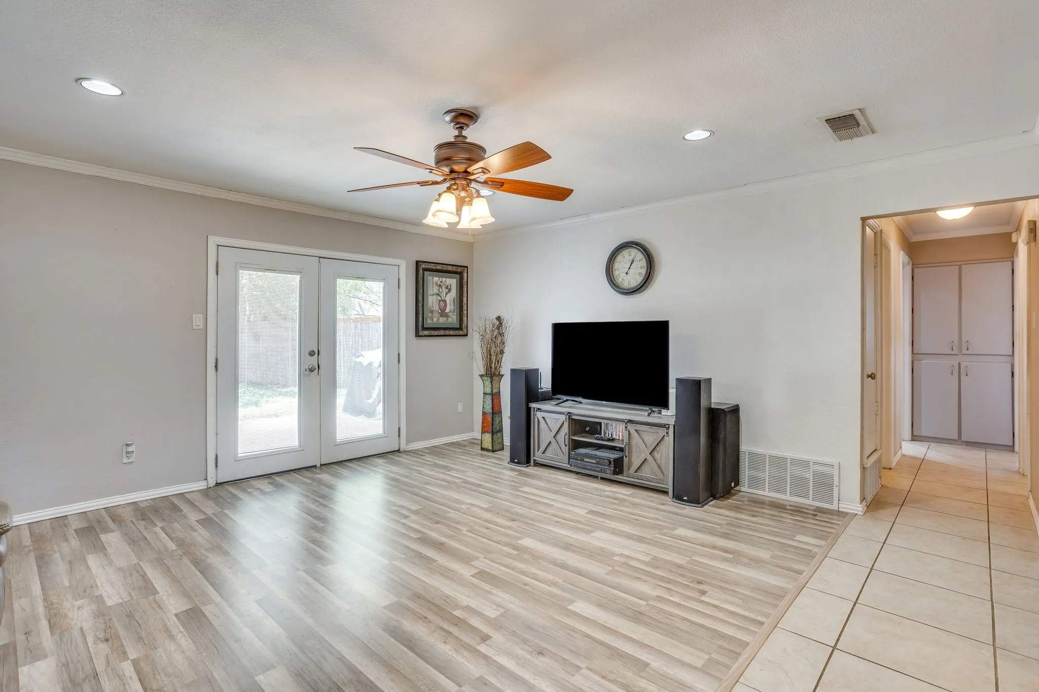 Spacious open-concept living area showcasing wood-finish flooring throughout, a ceiling fan with integrated lighting, recessed ceiling lights, and a media console with shelving