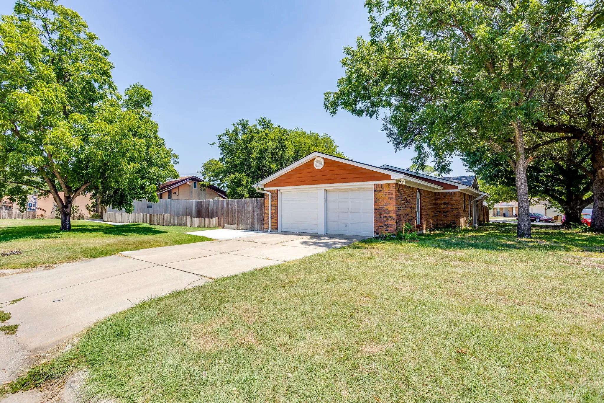 Charming brick home situated on a spacious, tree-lined lot featuring a two-car garage with white overhead doors and a concrete driveway